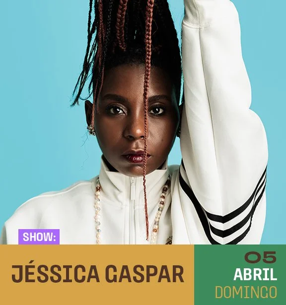 Retrato de uma mulher com cabelo trançado, usando jaqueta branca com faixas pretas, brincos e colar, com fundo azul.