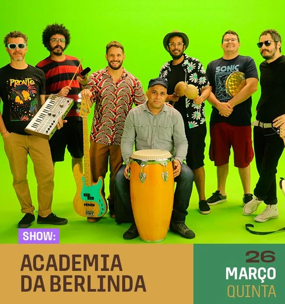 Grupo de sete pessoas segurando instrumentos musicais, posando em frente a uma parede verde, promovendo o show "Academia da Berlinda" em 26 de março, quinta-feira.