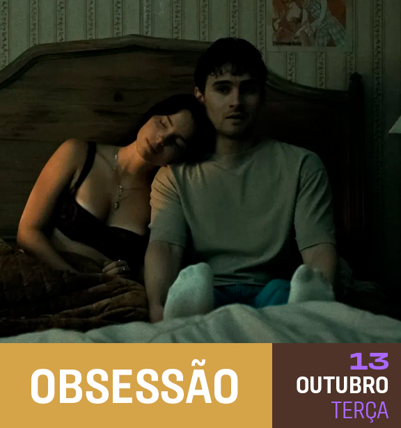 Um casal sentado na cama, com expressão séria, em um quarto com papel de parede padrão, com uma pessoa descansando a cabeça no ombro da outra.