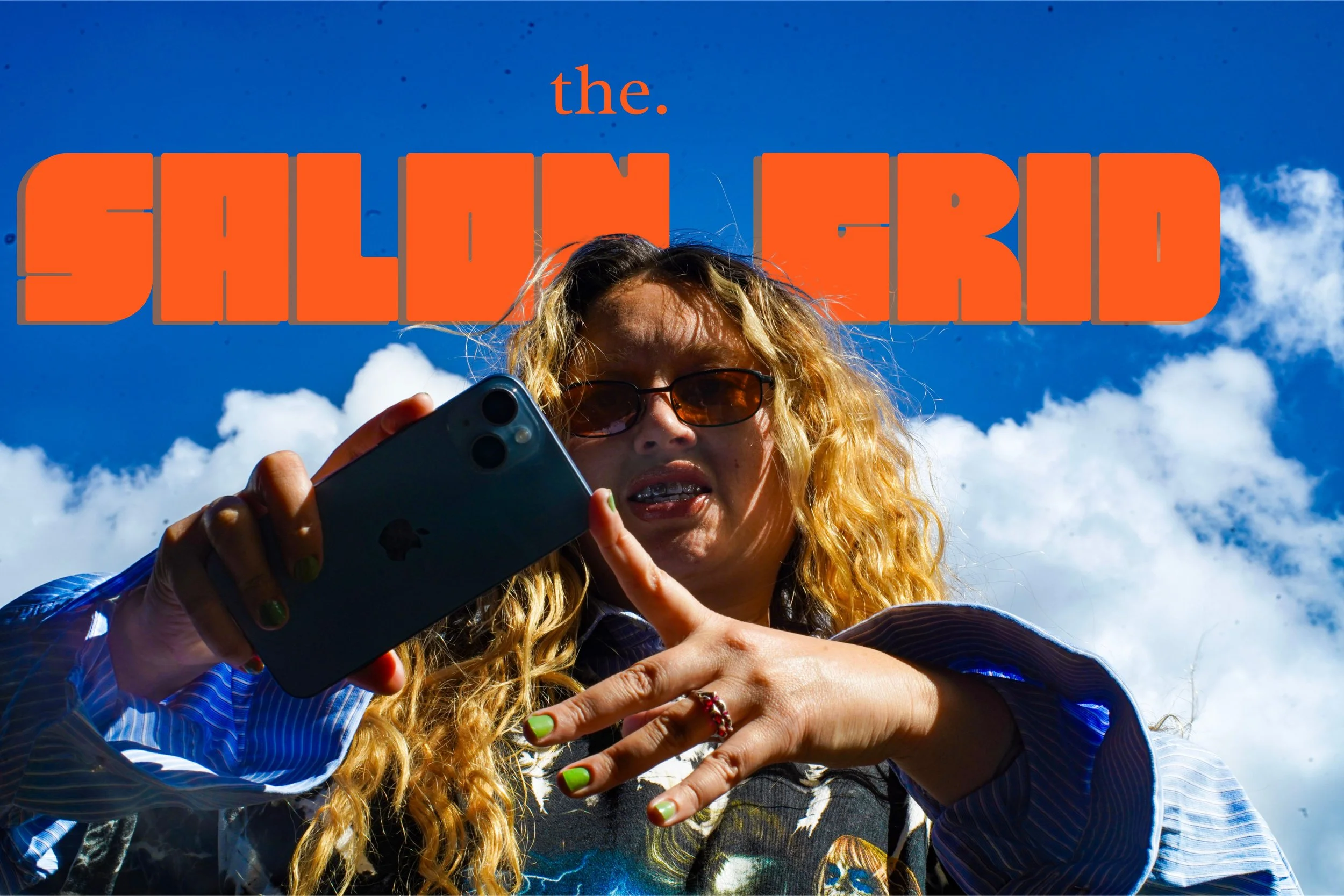 A woman with blonde curly hair and sunglasses, taking a selfie with a smartphone, against a bright blue sky with clouds, with large orange text reading 'the SALON GRID' above her head.