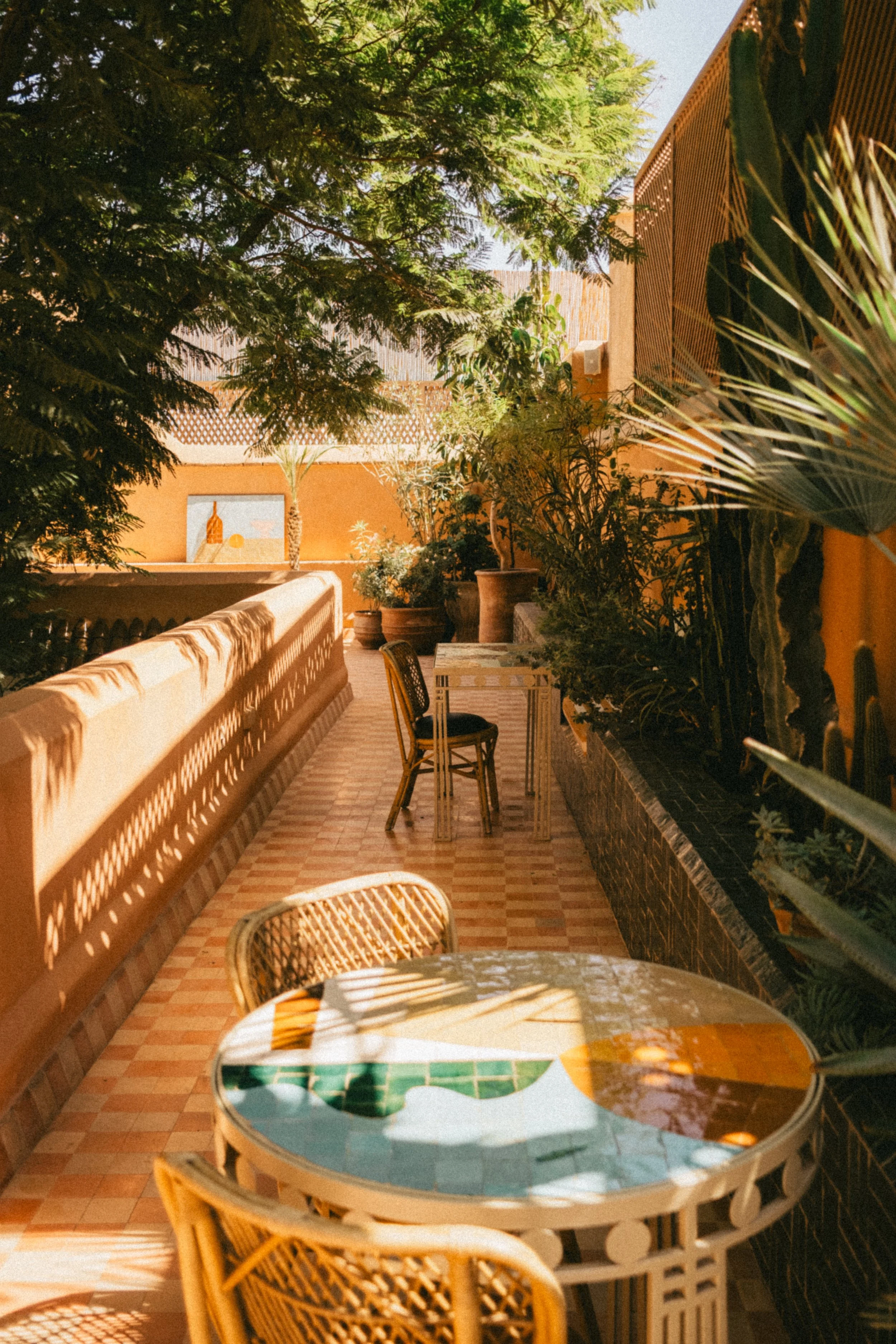 Terrasse en plein air avec des meubles en rotin, des plantes vertes et des murs orange ensoleillés.