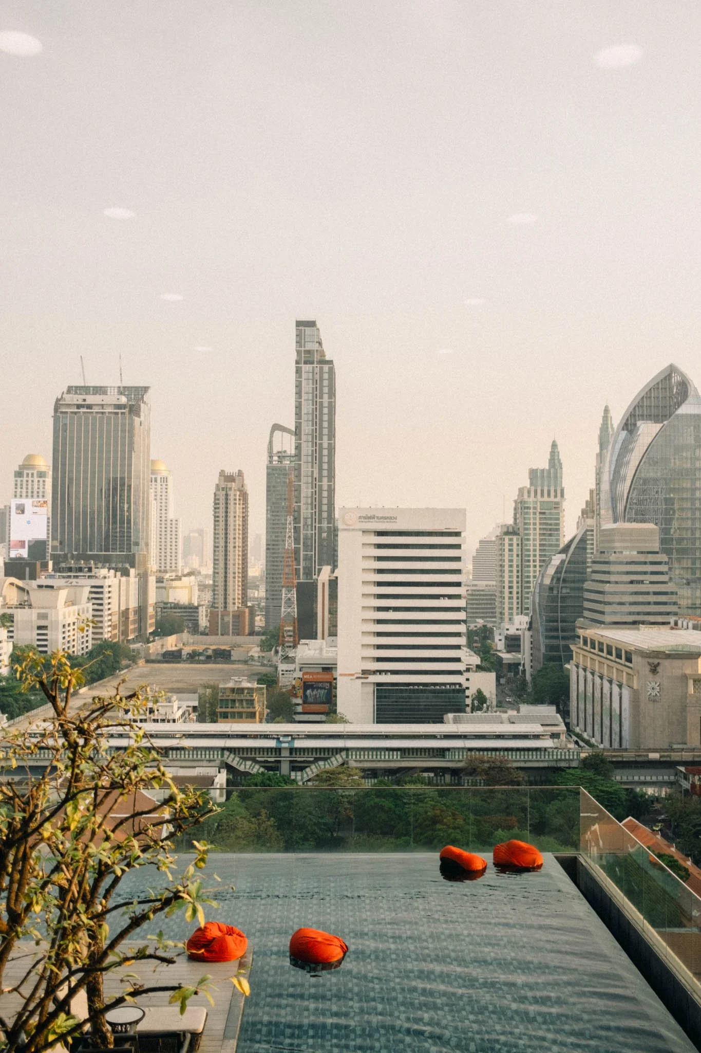 Vue de la ville moderne avec gratte-ciel sur fond de ciel clair, vue depuis une piscine en hauteur avec quelques oreillers flottants de couleur orange.