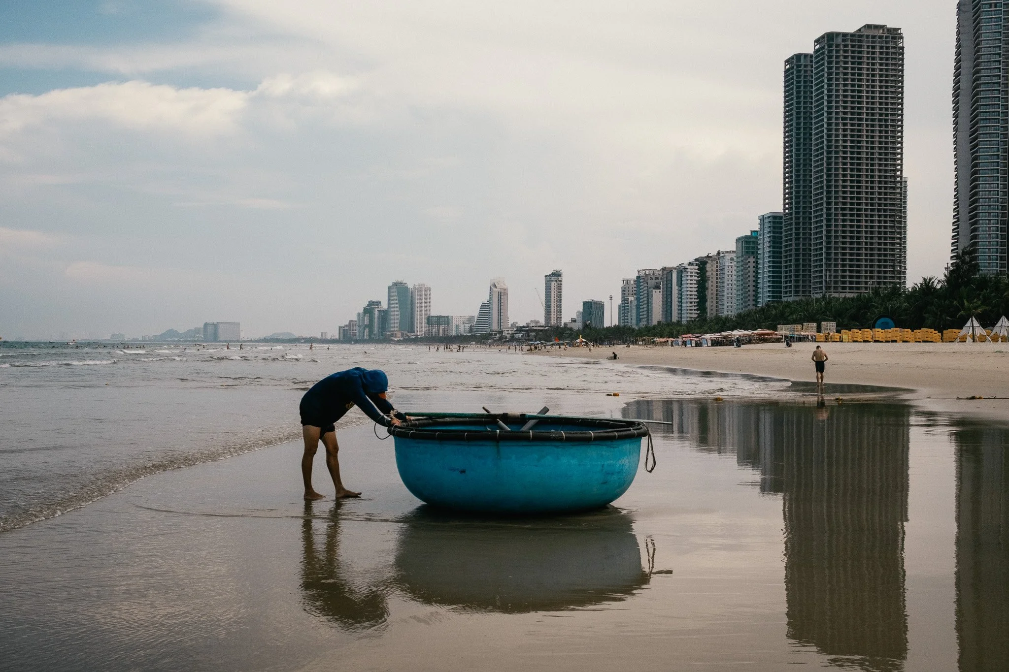 Personne en short et t-shirt ajustant une boule en plastique flottante sur la plage, avec un horizon de gratte-ciel urbains en arrière-plan.