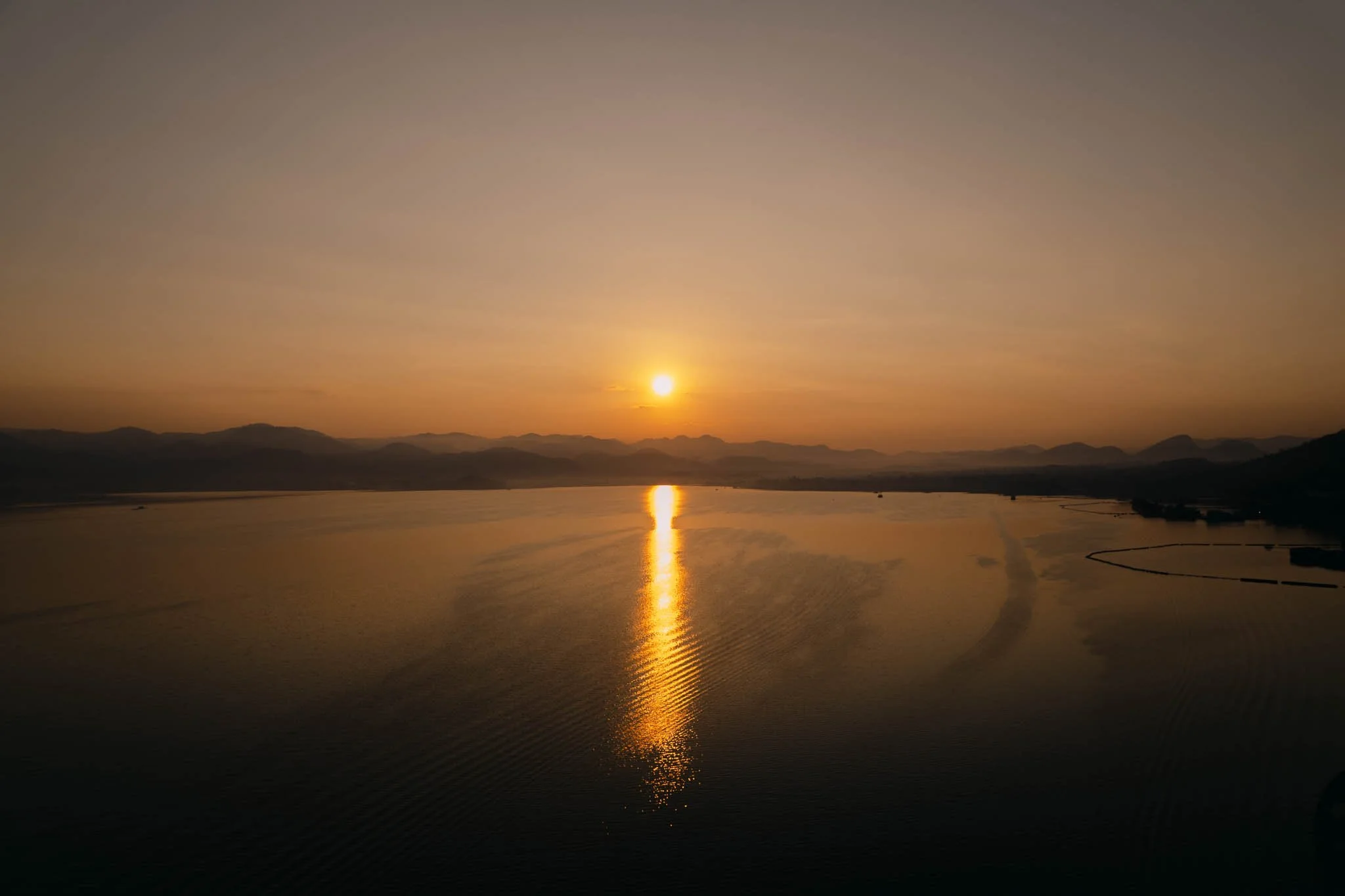 Coucher de soleil sur un lac avec des montagnes en arrière-plan, reflet du soleil sur l'eau.