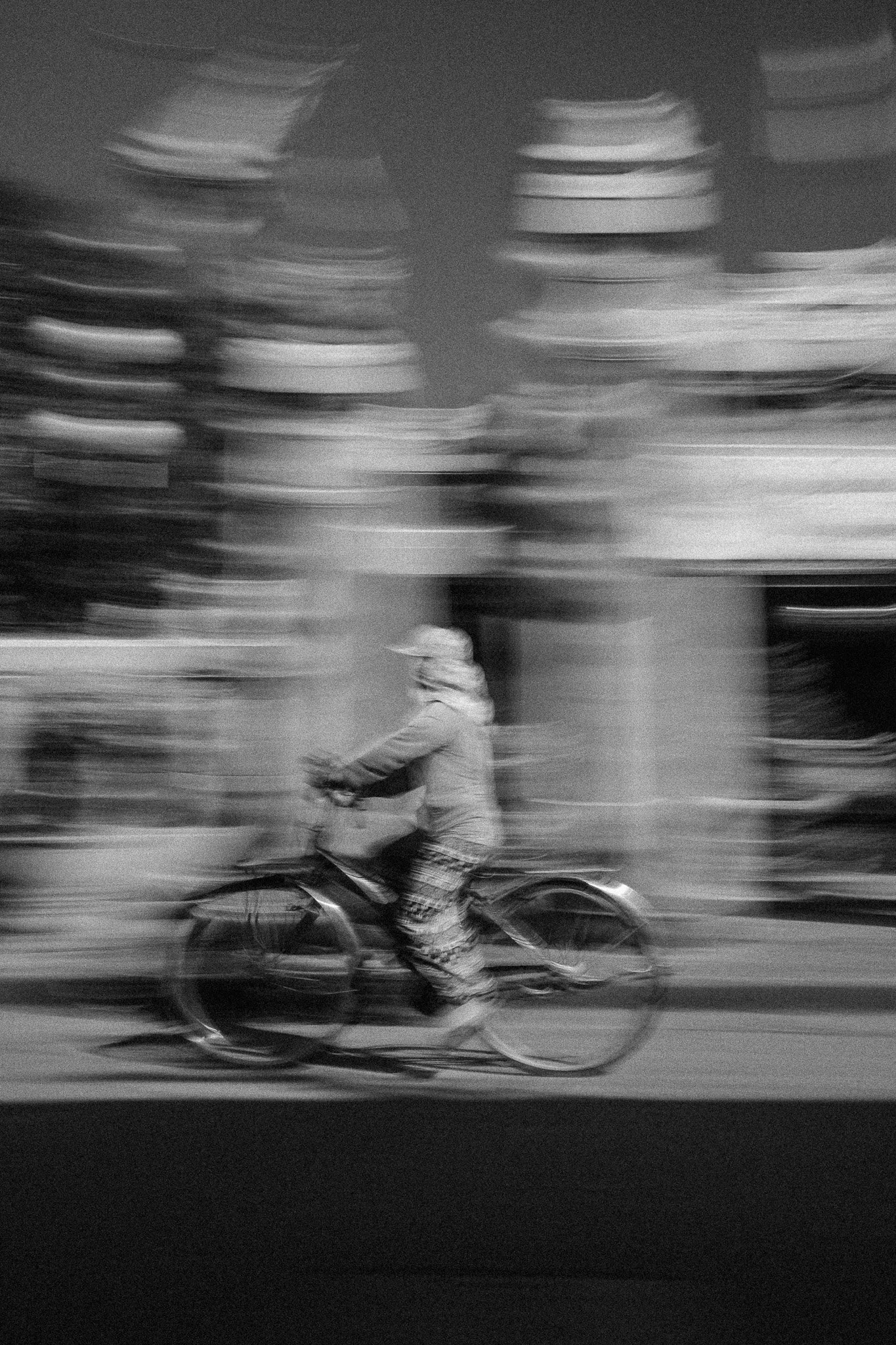 Un homme en manteau et pantalons à motifs roulant à vélo en mouvement dans une rue urbaine, flou de mouvement.