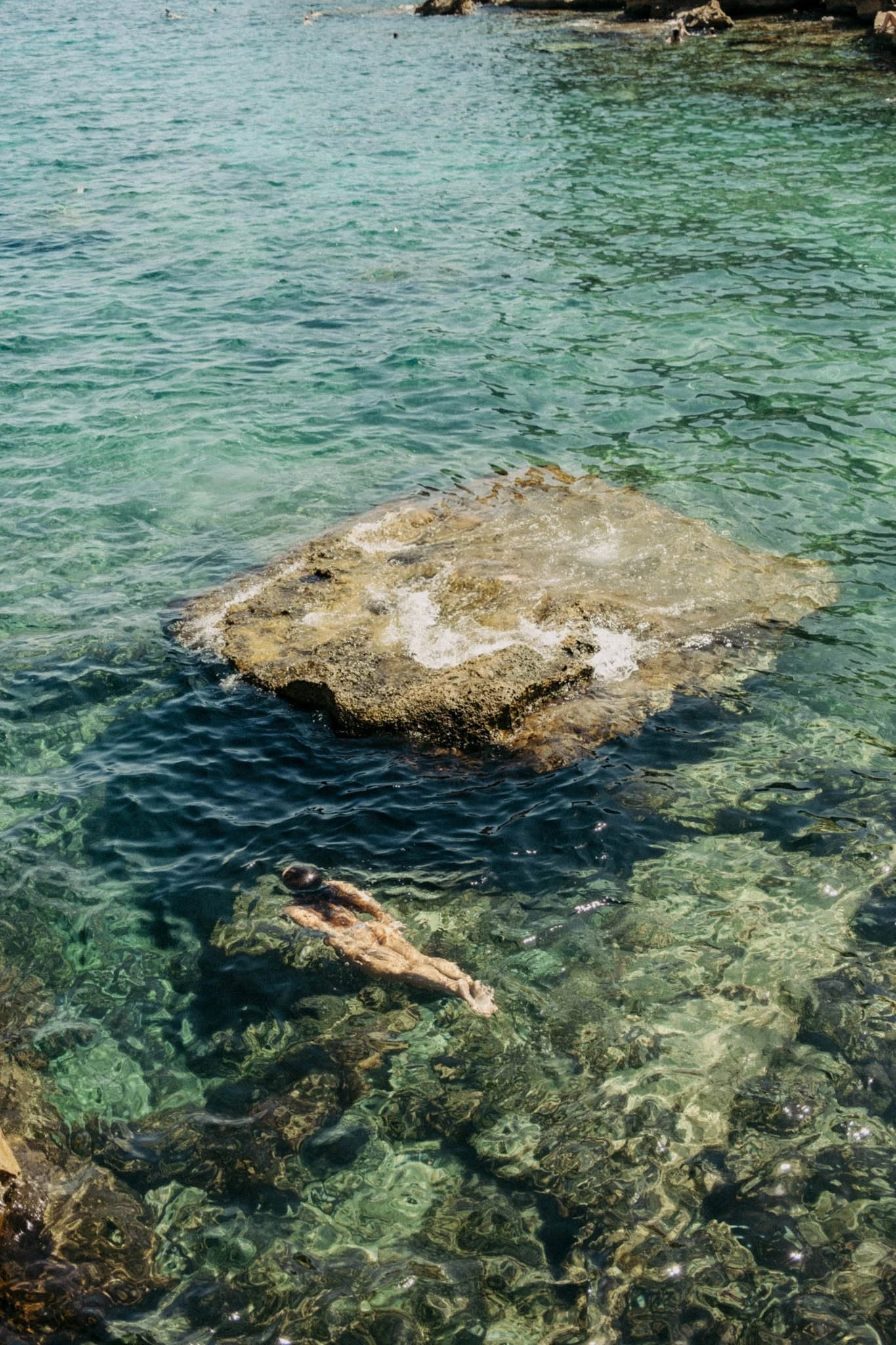Une roche visible dans une eau claire de mer turquoise, avec un mannequin flottant en dessous.