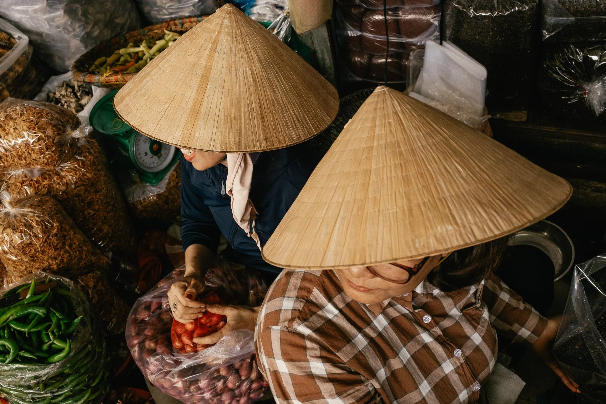 Deux femmes portant des chapeaux coniques en bambou vendant des légumes dans un marché.