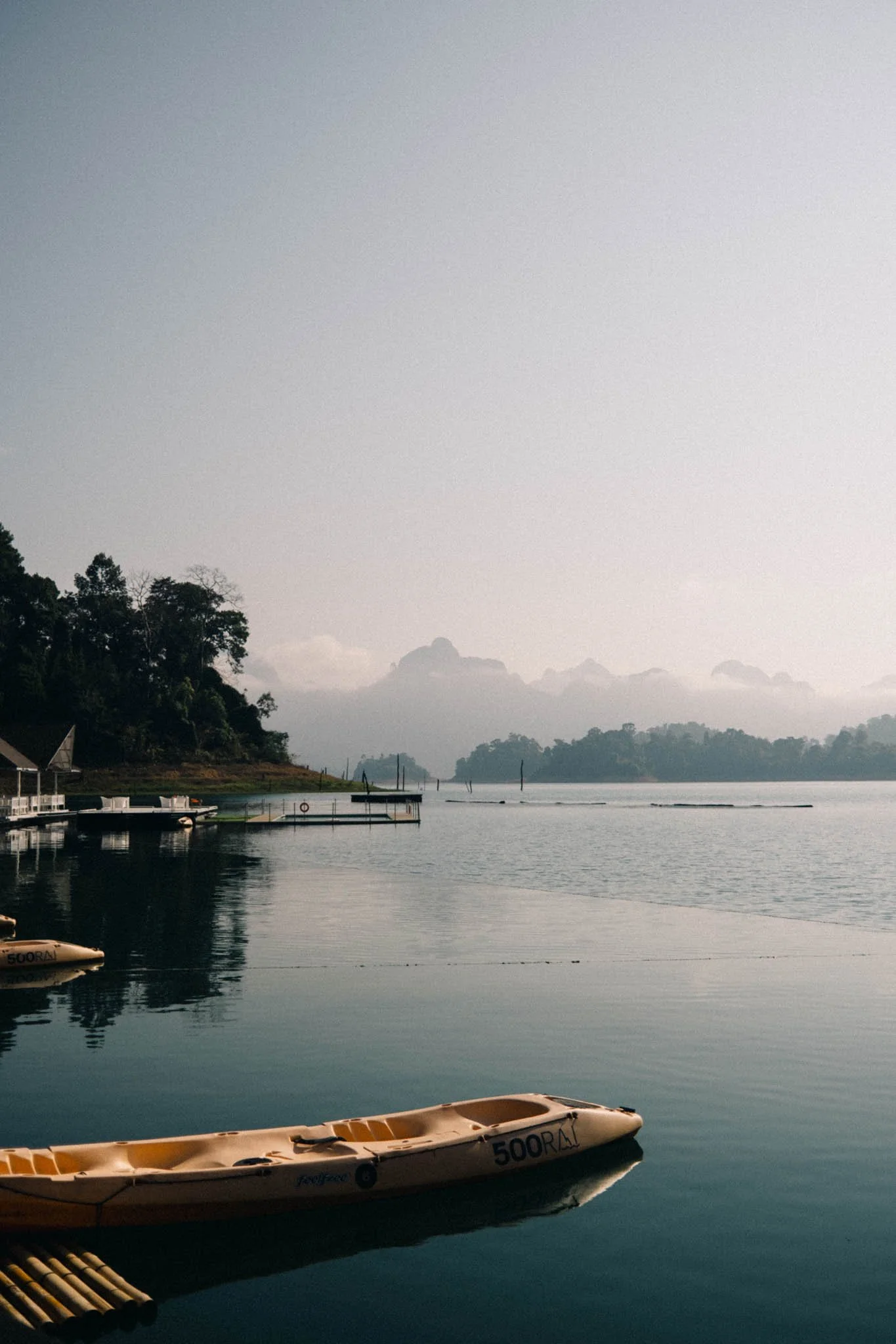 Une vue paisible d'un lac entouré de collines verdoyantes et de montagnes au fond, avec un kayak orange flottant à la surface de l'eau.