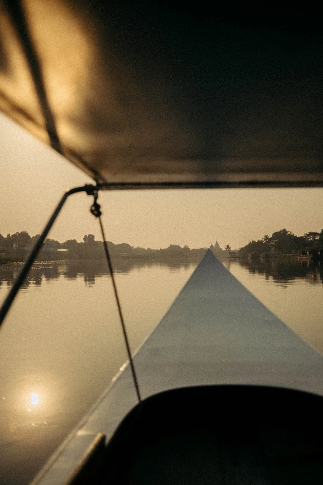 Vue depuis le cockpit d'un bateau à moteur, naviguant sur une rivière calme au crépuscule, avec les silhouettes de bâtiments et de palmiers à l'horizon.