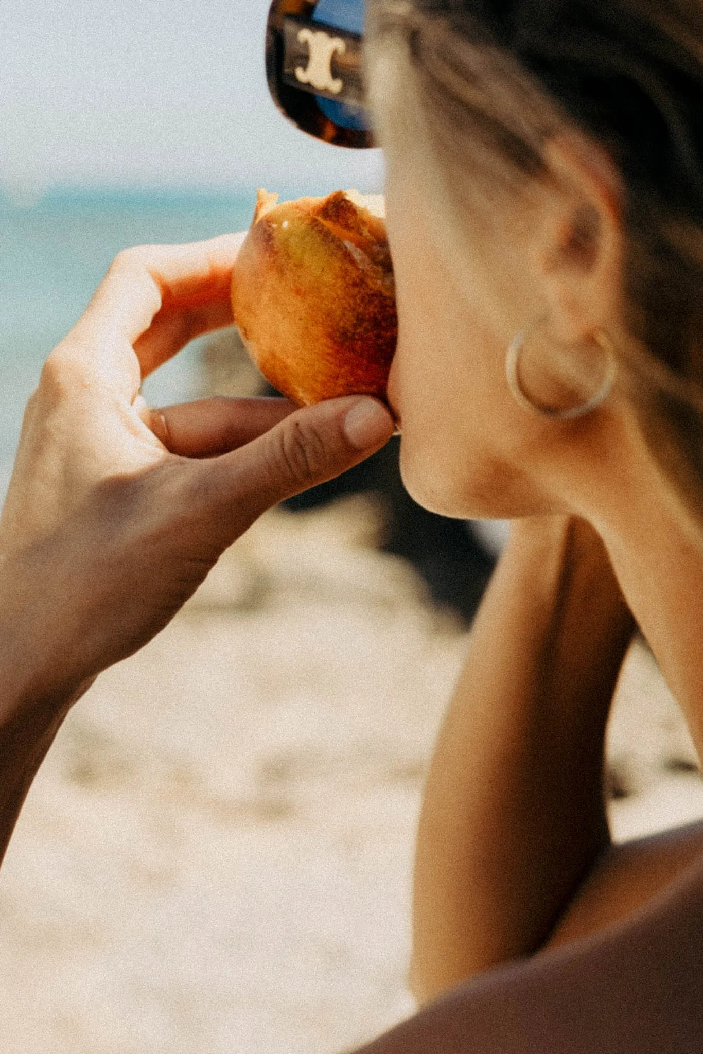 Une femme qui tient un pêcheur près de sa bouche, avec la mer en fond.
