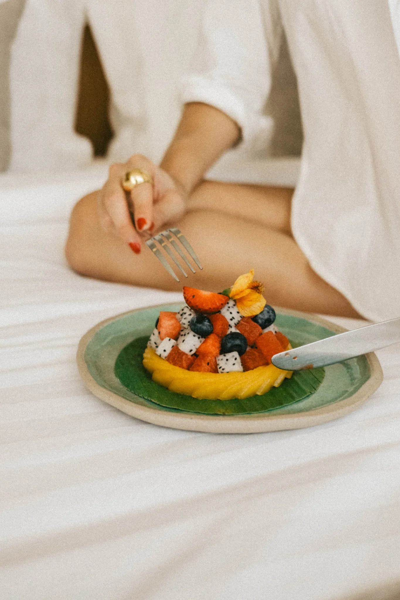 Femme mangeant une assiette de fruits exotiques, incluant mangue, fraise, kiwi, myrtilles et fruit du dragon.