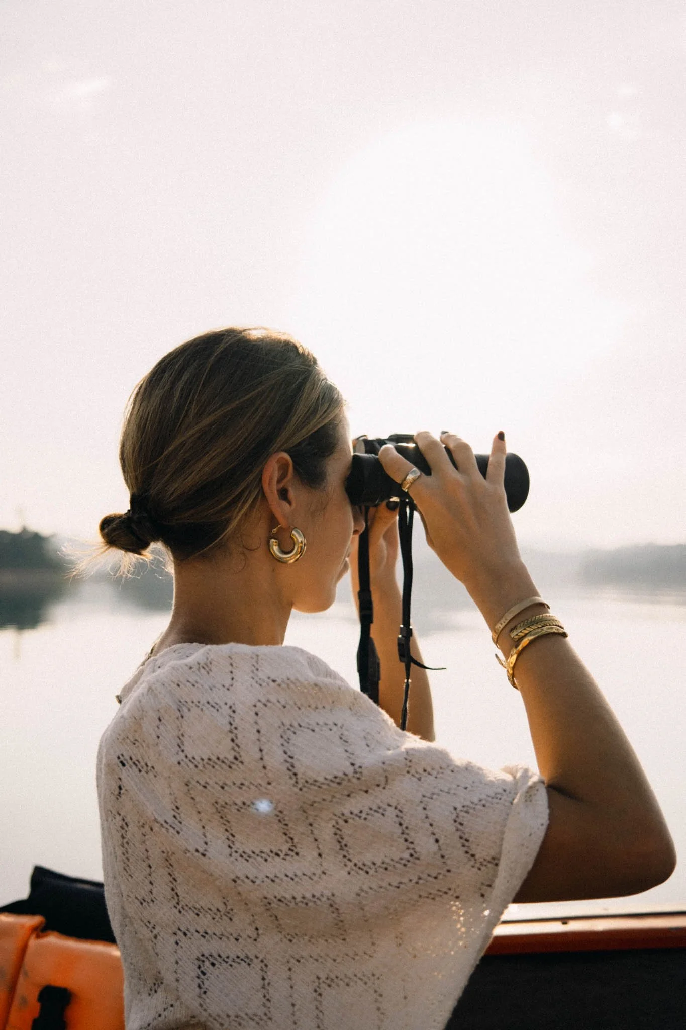 Femme regardant à travers des jumelles près d'un plan d'eau, lors d'un coucher de soleil.