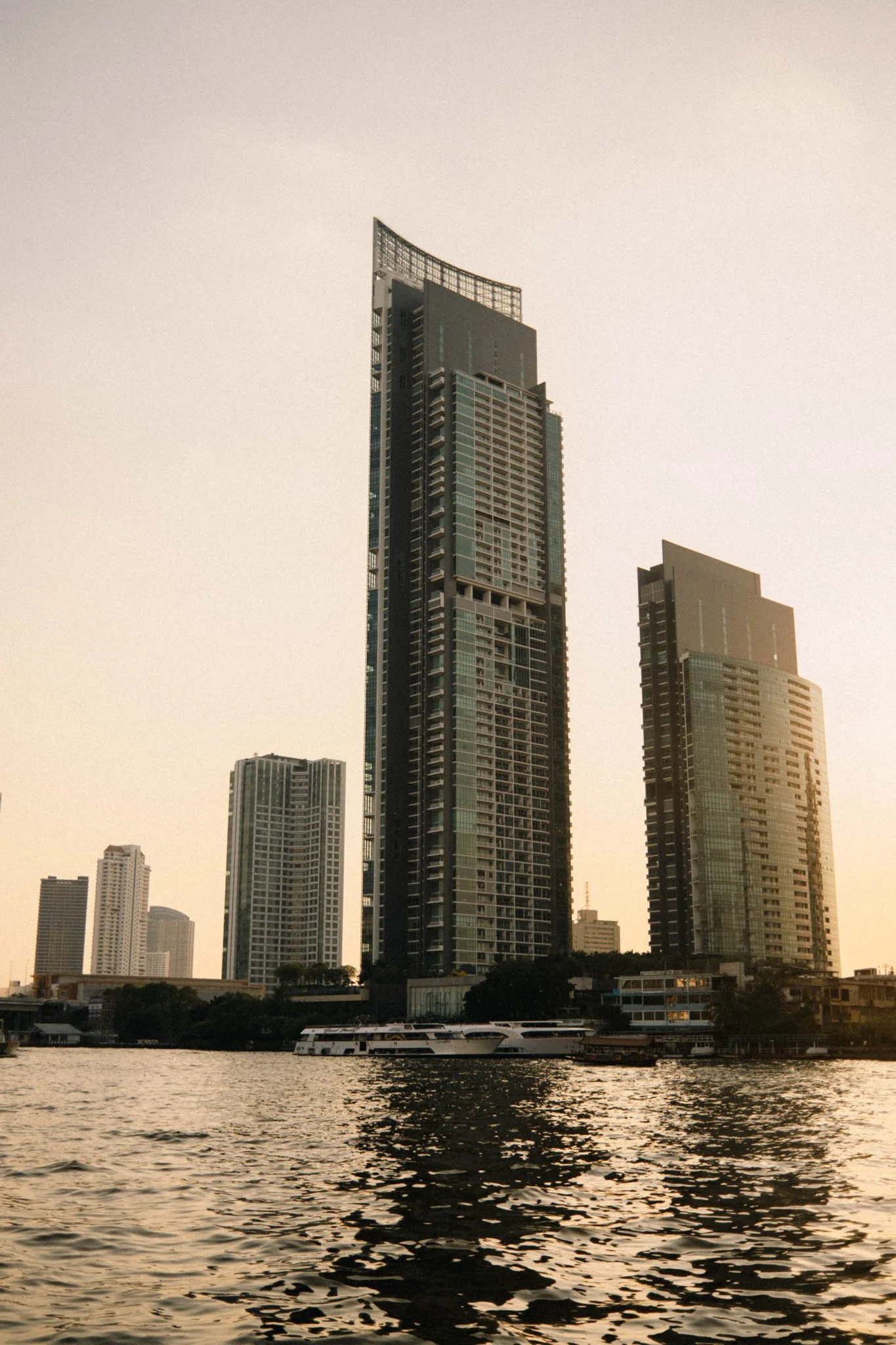 Gratte-ciel modernes le long d'une rivière au coucher du soleil, avec des yachts amarrés au premier plan.
