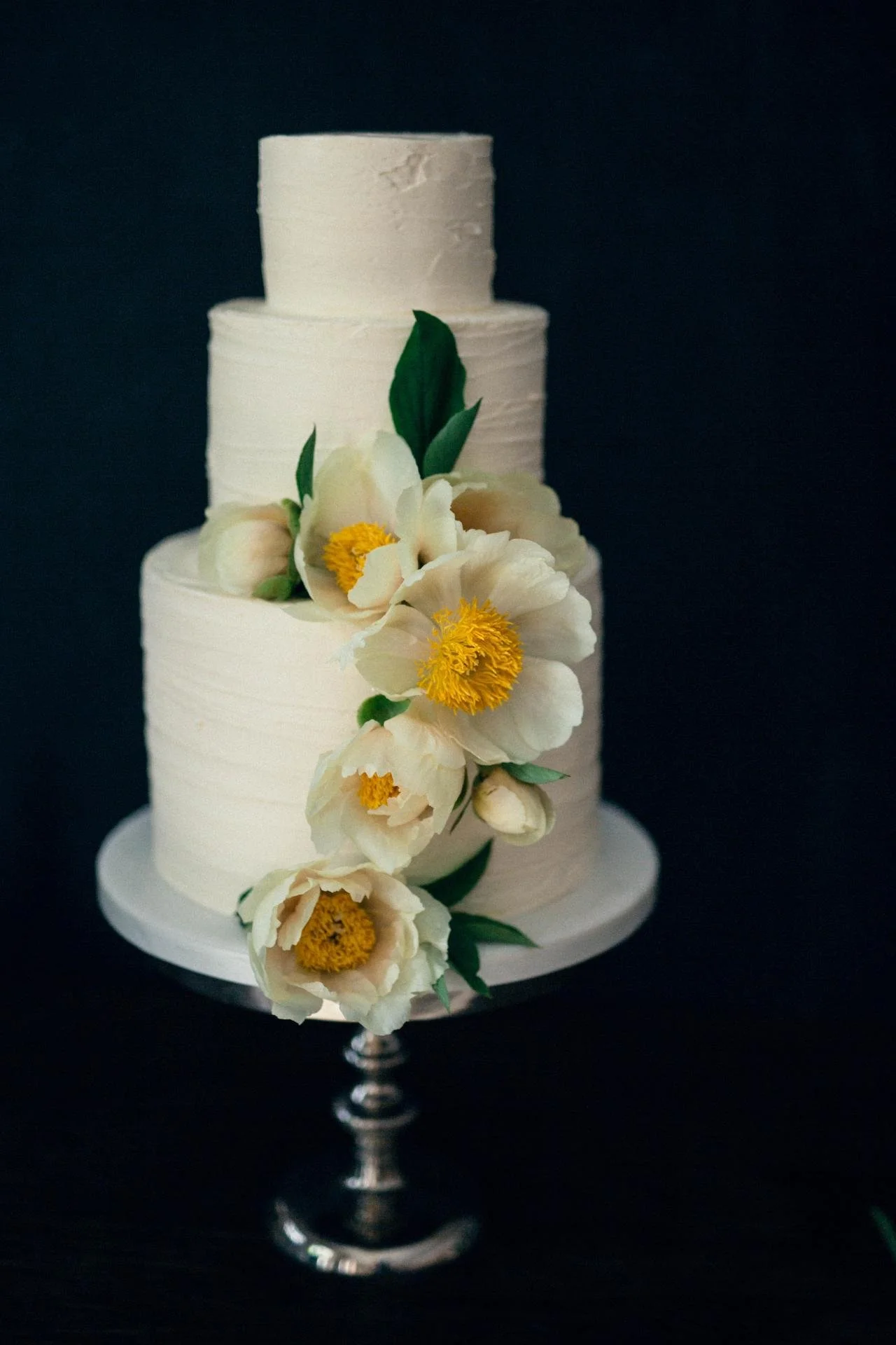 White floral wedding cake decorated with large cream flowers and fresh green leaves