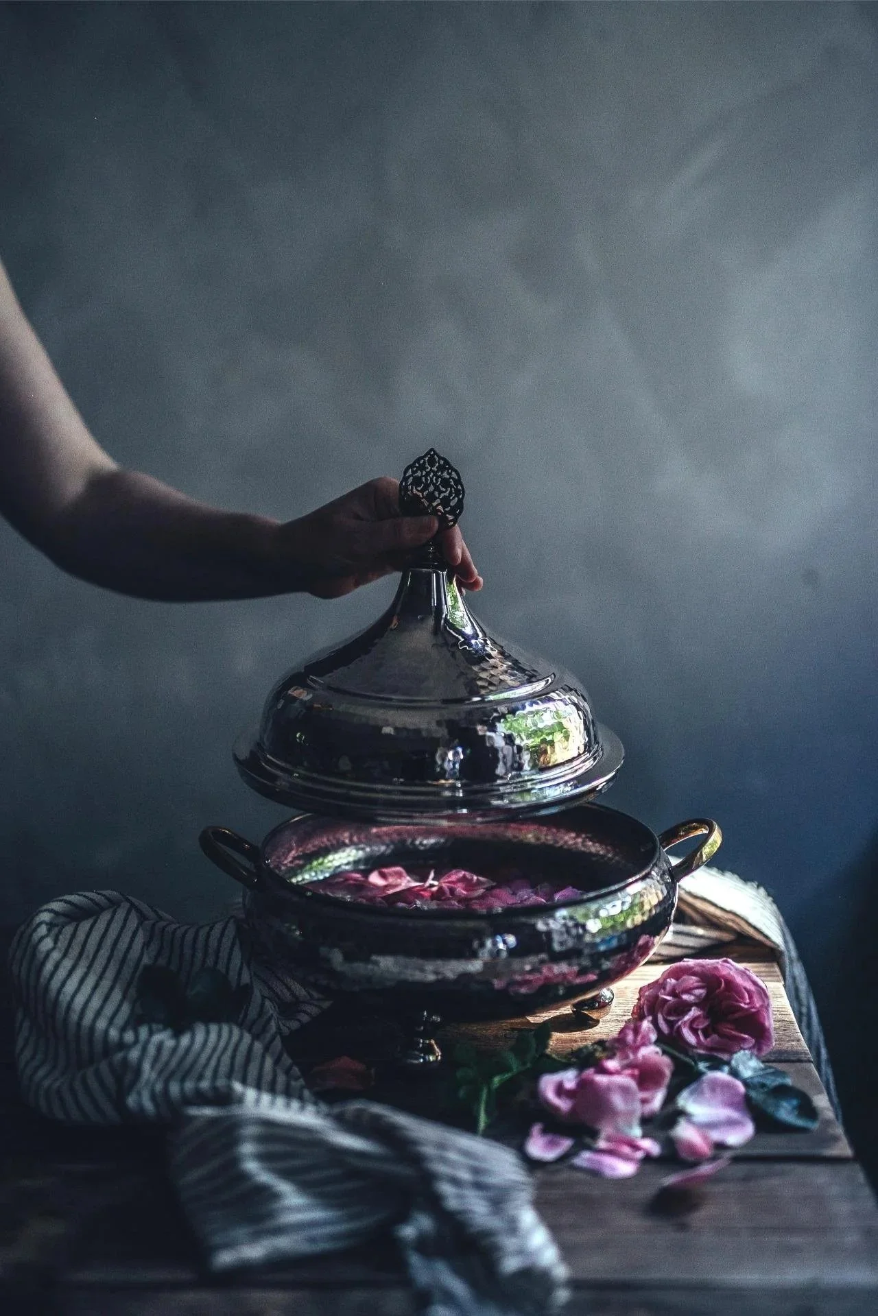 Elegant dark floral arrangement with silver serving dish and rose petals