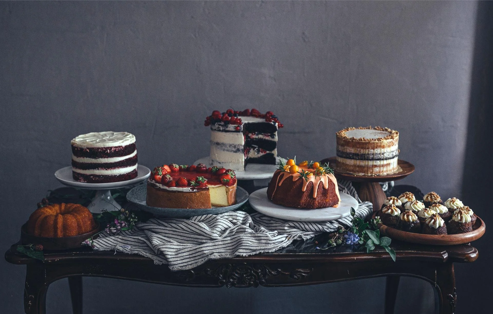 a cake table displaying covered cakes topped with fruits and creamy cupcakes at dilekerei bakery in berlin