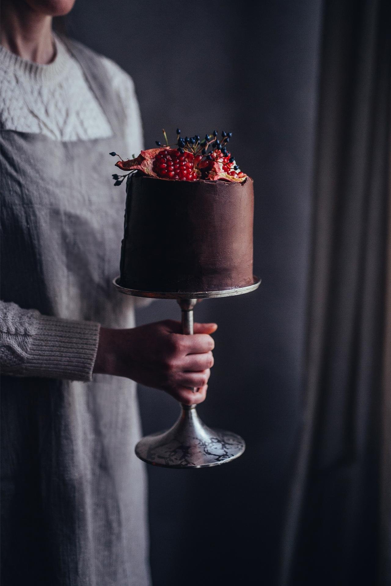 Dark chocolate birthday cake topped with fresh berries on an elegant cake stand