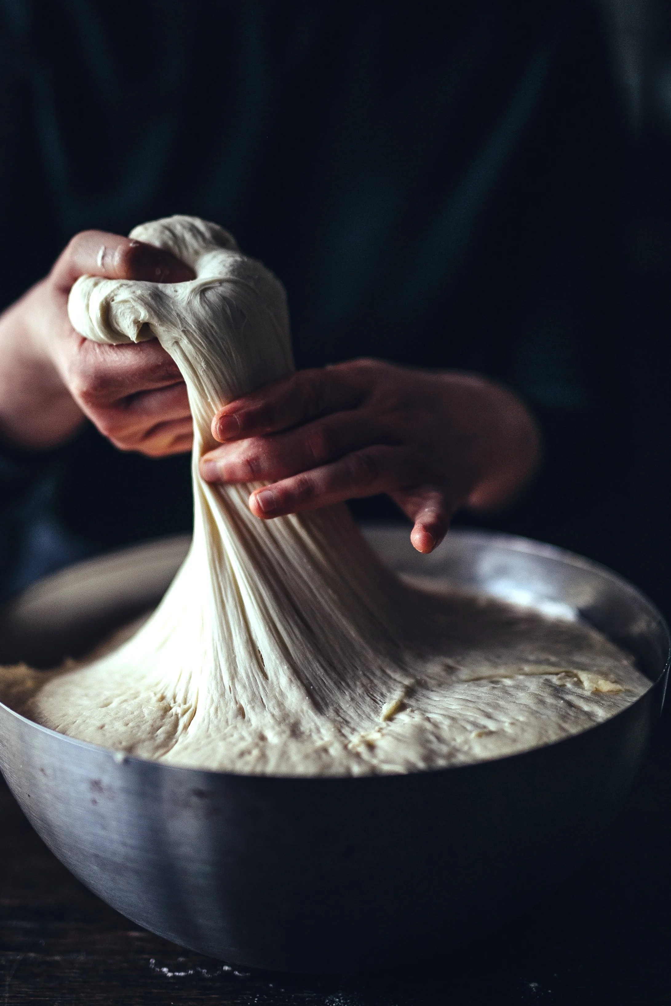 Close-up of hands stretching dough in a round baking pan.