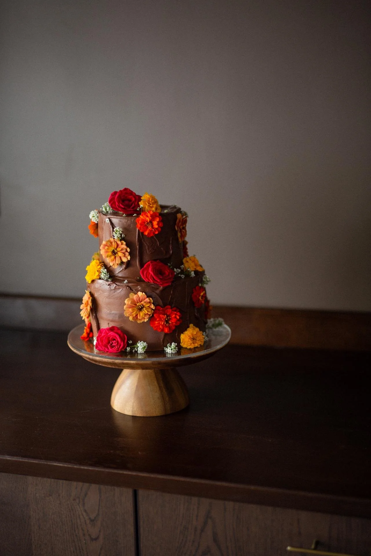 Dark floral wedding cake decorated with vibrant red, orange and pink flowers