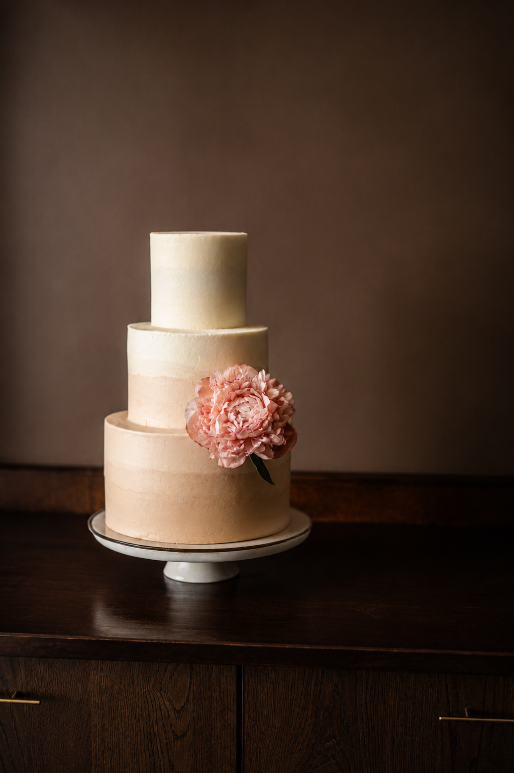 Minimal two-tier wedding cake in neutral tones with a soft pink floral arrangement