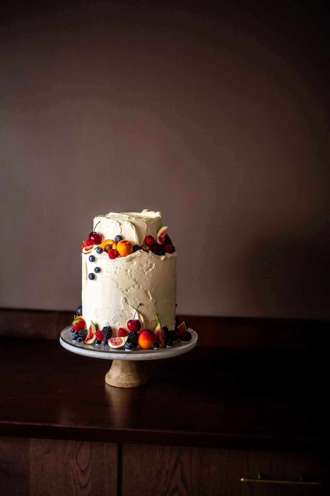 Rustic white wedding cake decorated with fresh red berries and buttercream