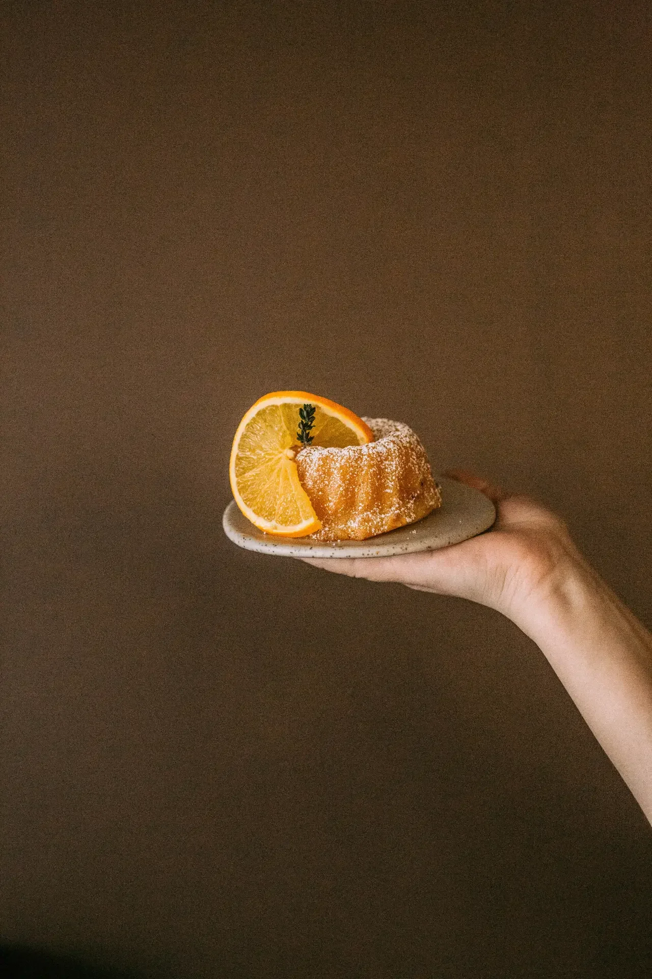 Hand holding orange mini bundt cake against warm textured wall in Dilekerei café