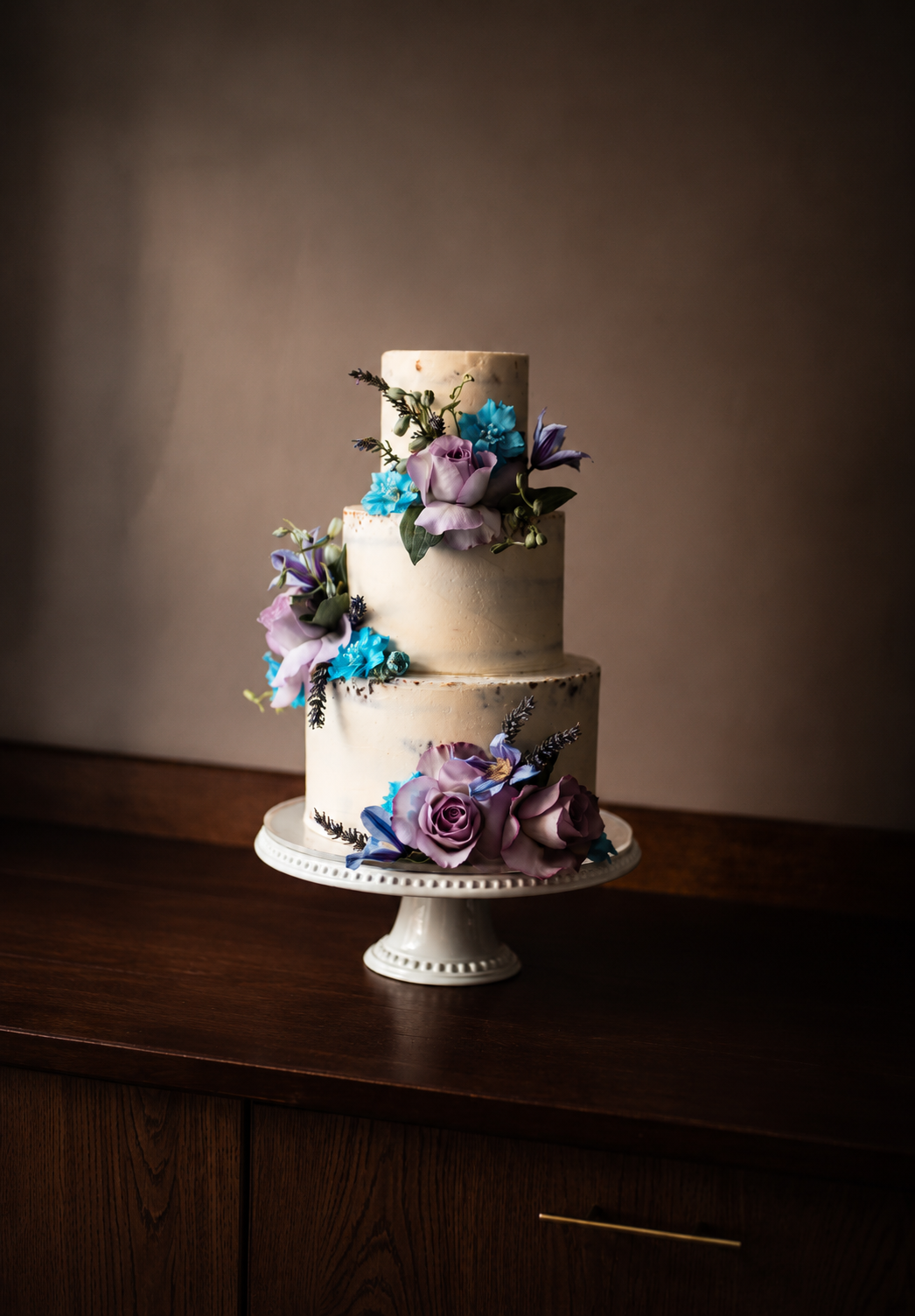 Two-tier floral wedding cake decorated with blue, purple and white seasonal flowers