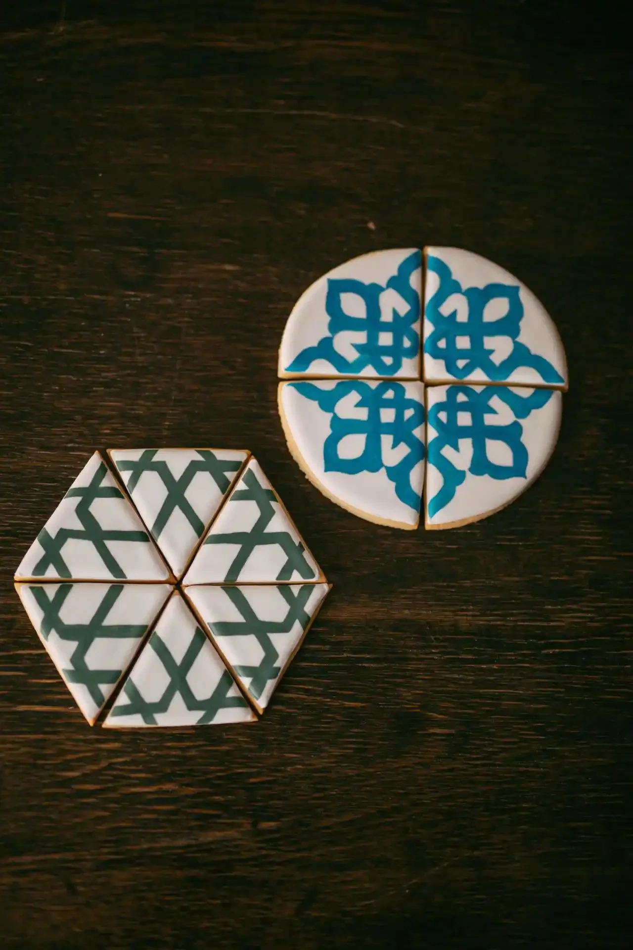 Two stacks of decorated cookies on a dark wooden surface, one with blue geometric patterns and the other with green interlocking lines.
