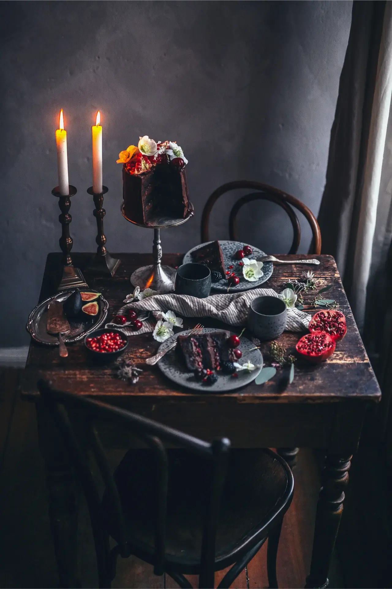 Chocolate celebration cake surrounded by candles, fruit and floral arrangements