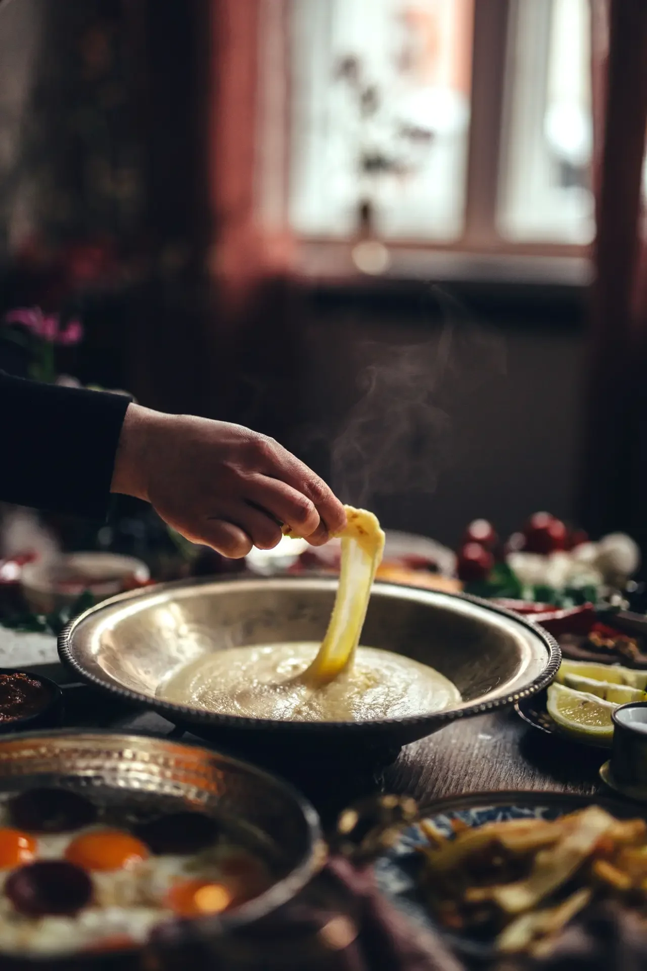 Hand dipping fresh flatbread into creamy mezze spread on traditional serving tray