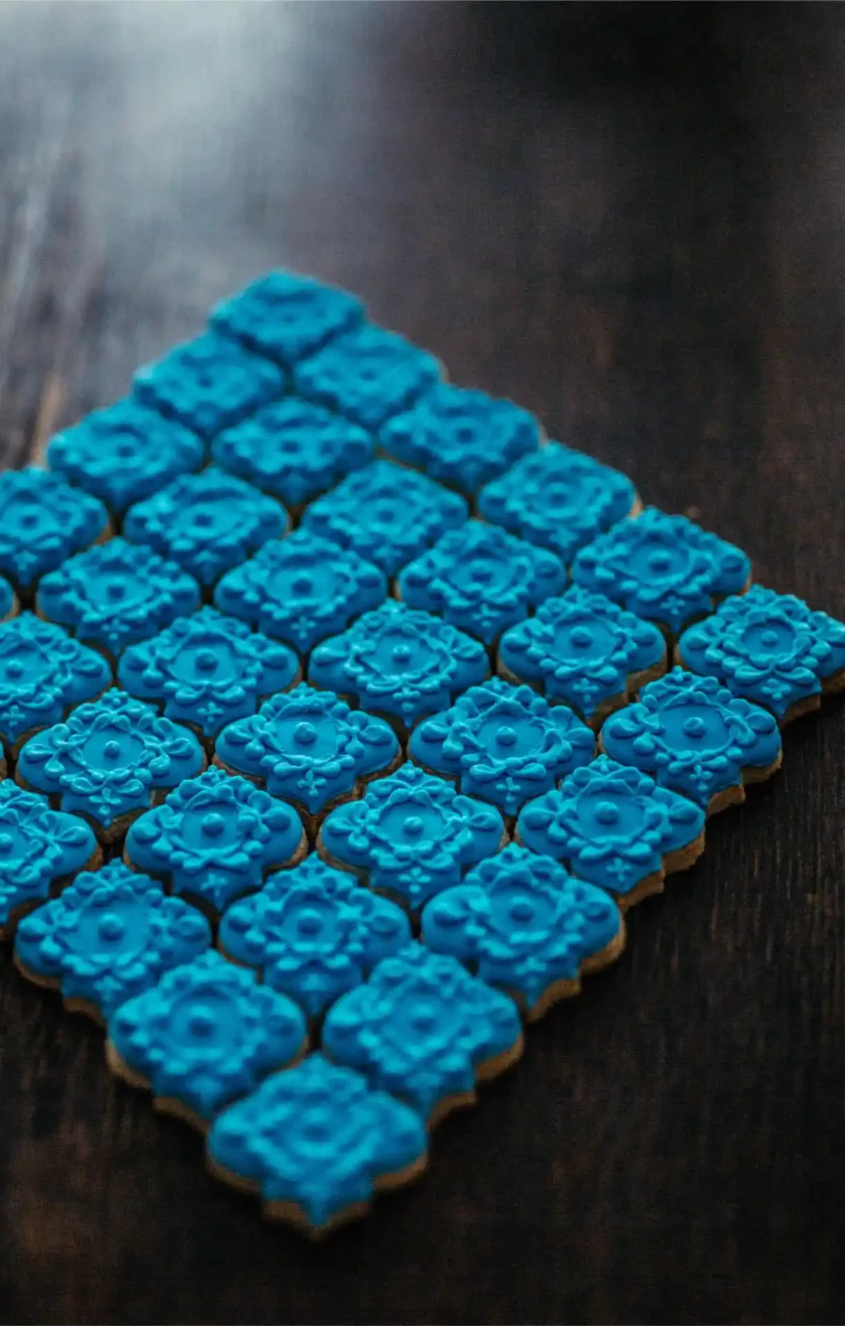 Close-up of multiple decorated cookies with blue icing, arranged in a pyramid shape on a dark surface.