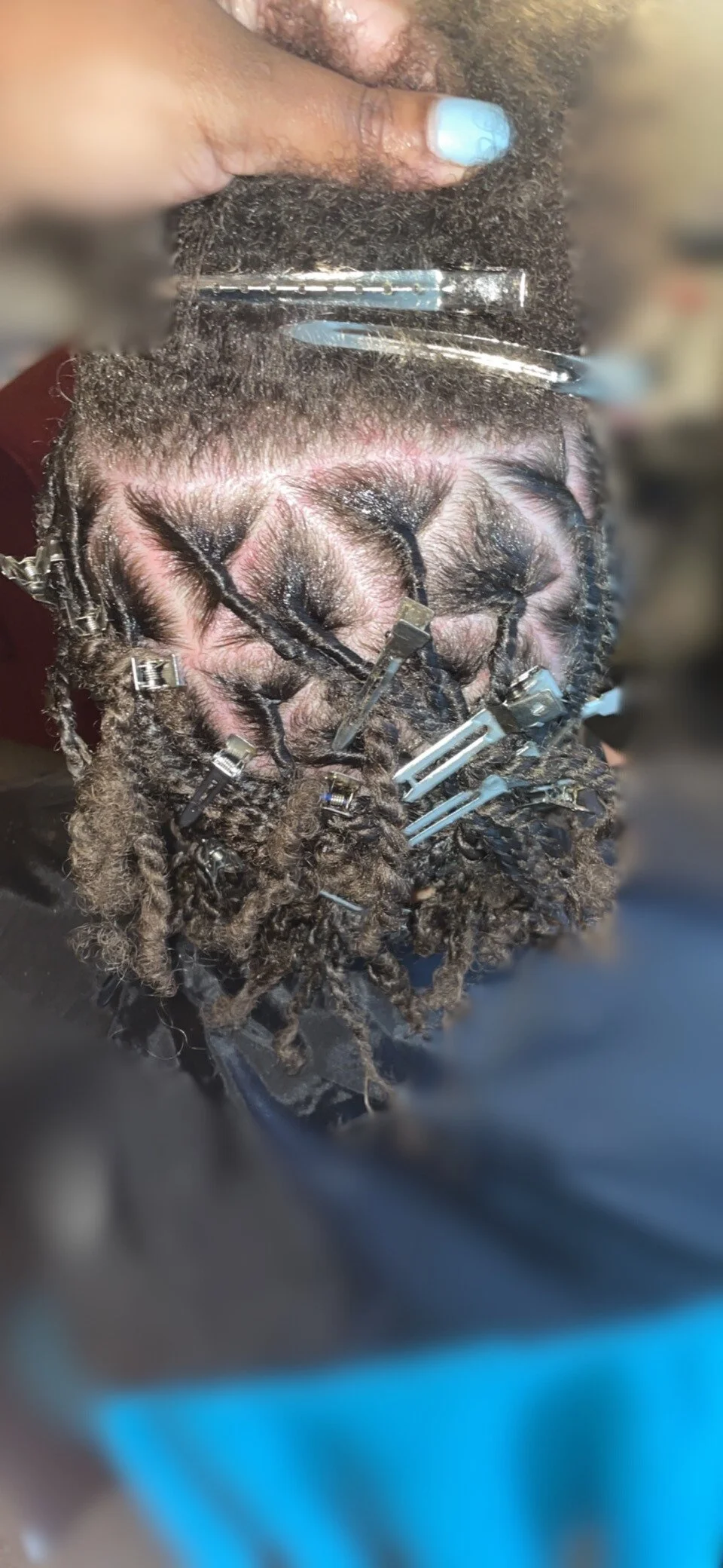 Close-up of hair being styled into locs with sectioning clips and products applied.