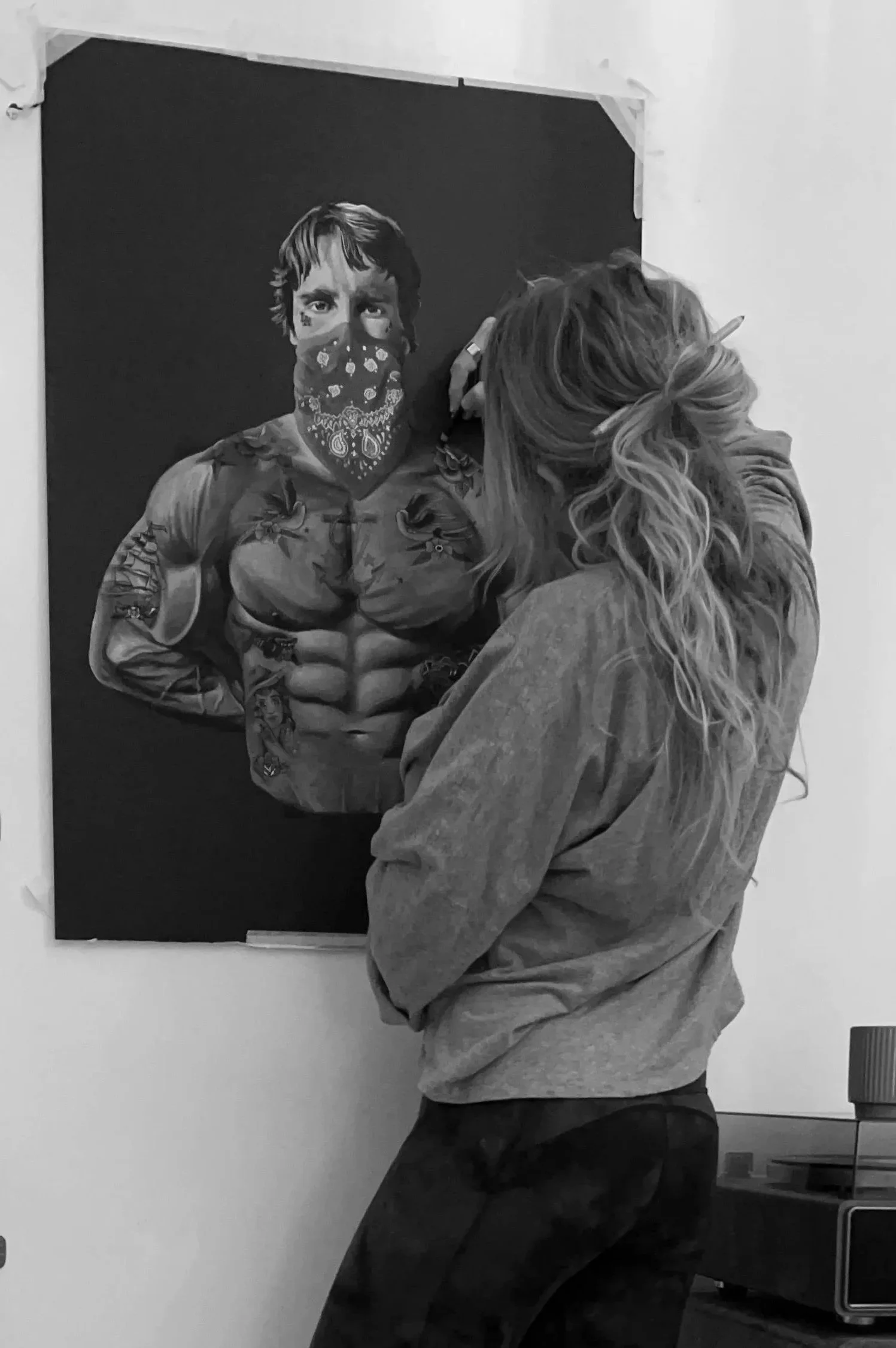 An artist drawing a realistic portrait of a muscular man with a bandana over his face, on a blackboard.