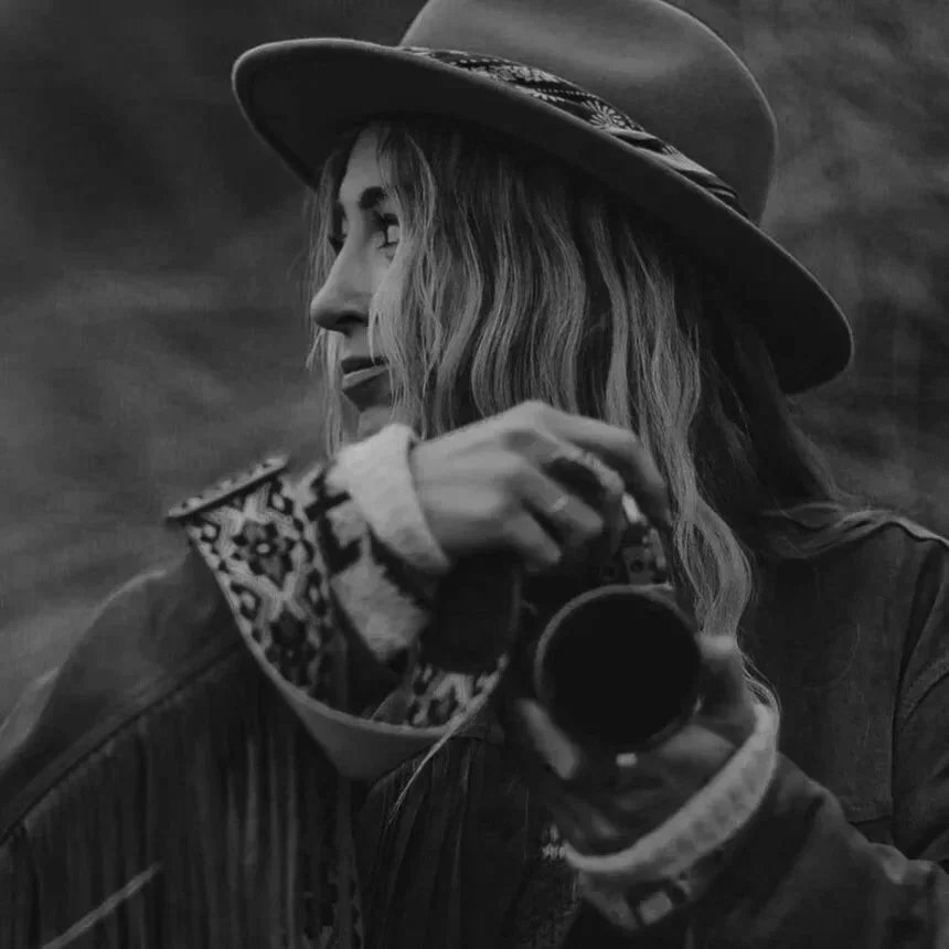 Black and white photo of a woman wearing a wide-brimmed hat, holding a cup, and looking off to the side.