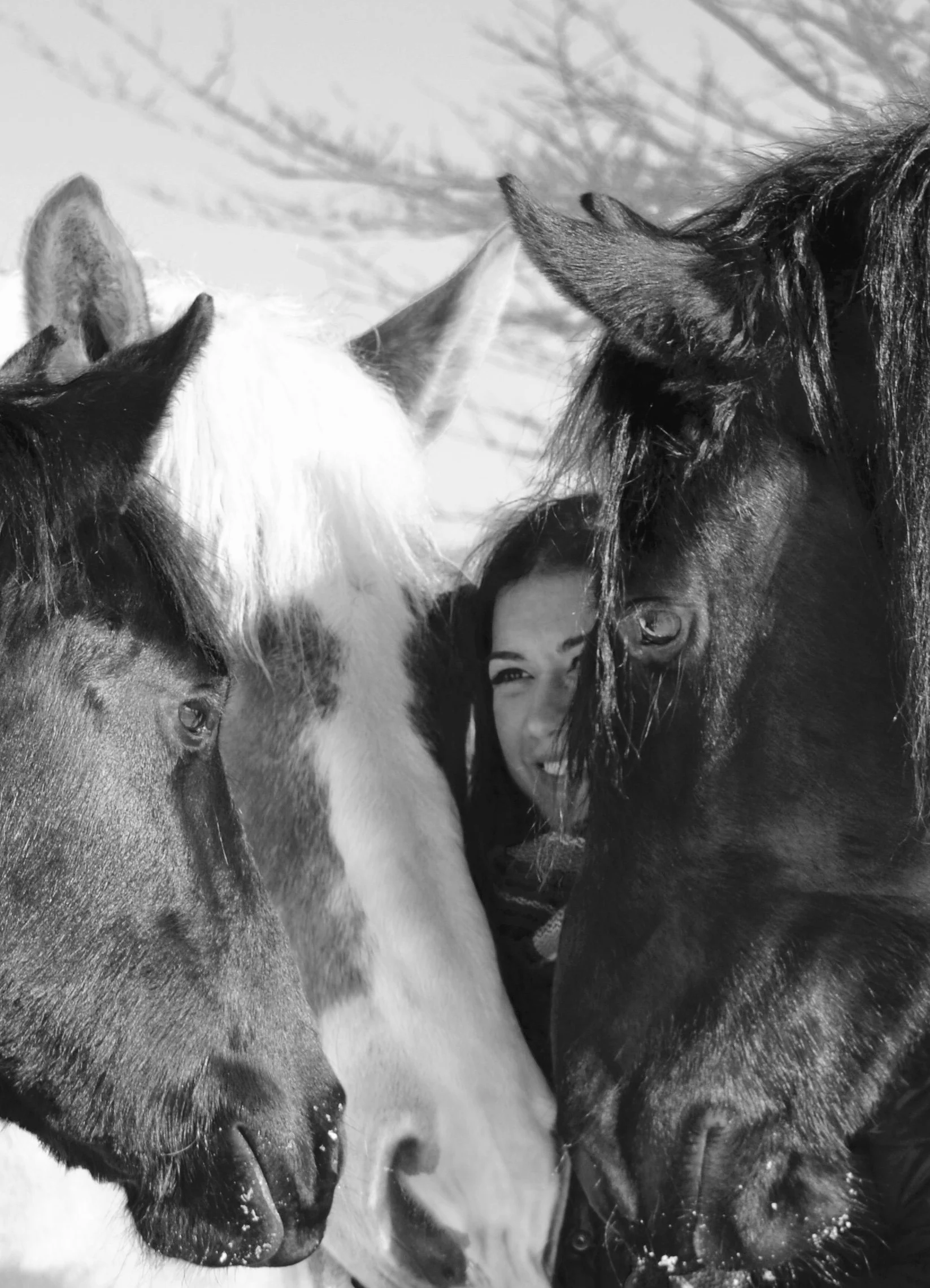 A woman smiling and surrounded by four horses, close-up of their heads.
