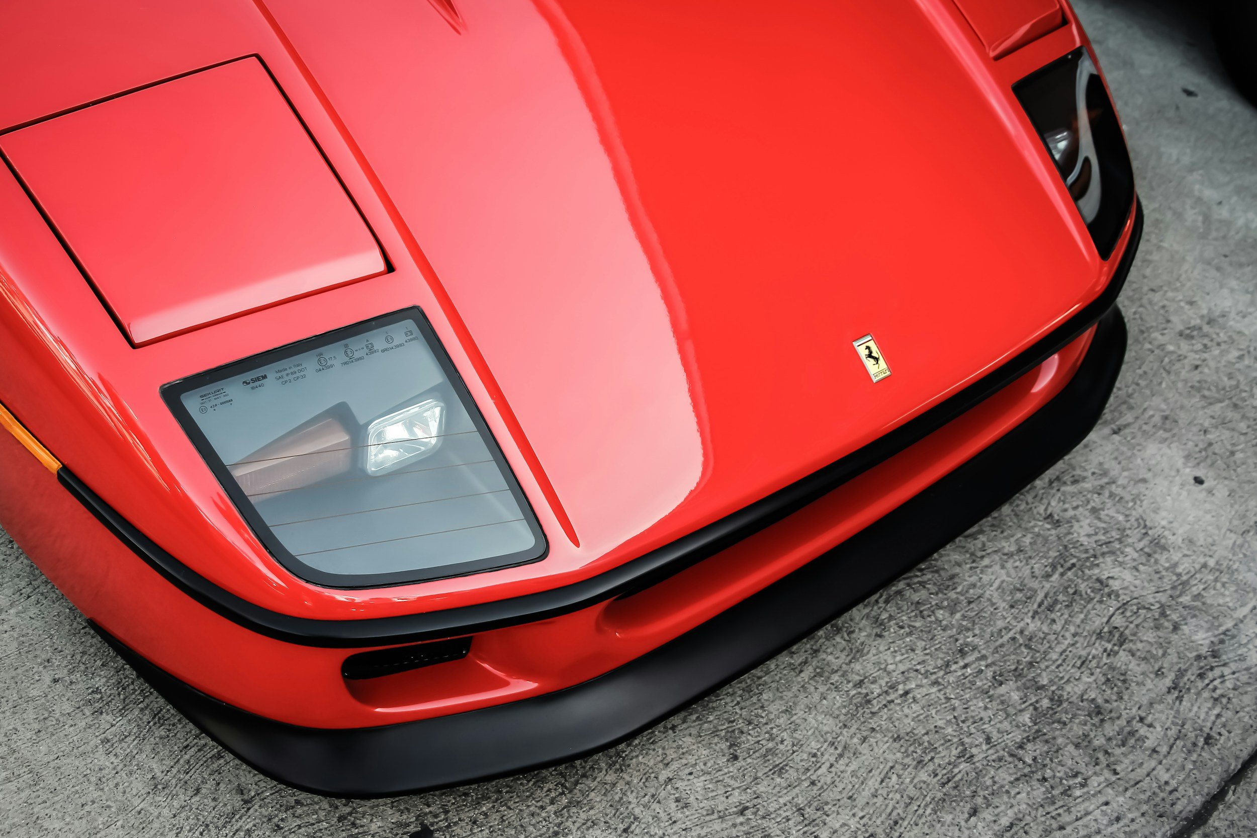 Close-up of front section of red Ferrari sports car showing headlight, hood, and windshield