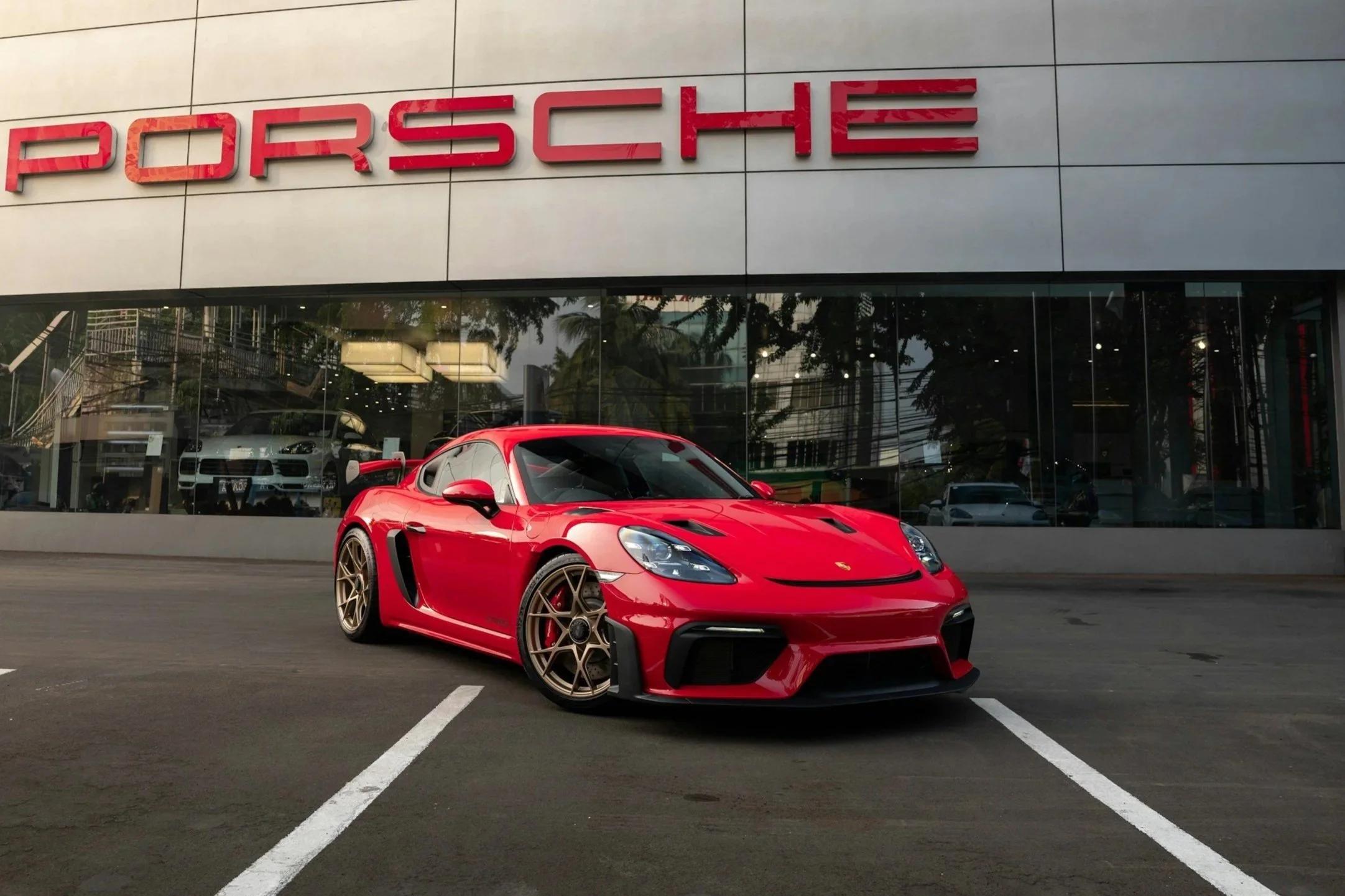 A red sports car parked in front of a Porsche dealership with large windows and a Porsche sign.