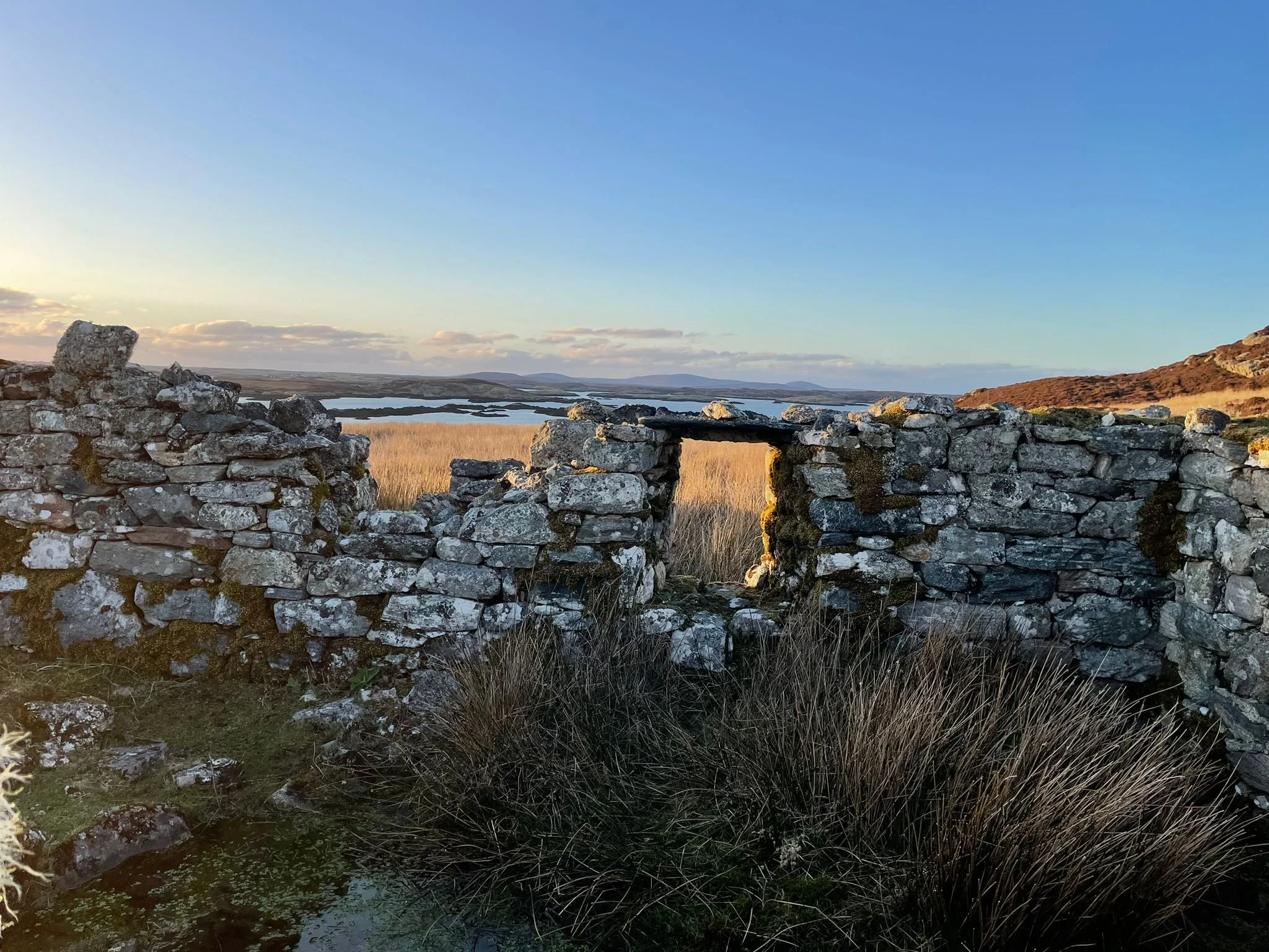 A stone wall with an opening overlooking a marshland and lakes under a blue sky at sunset.