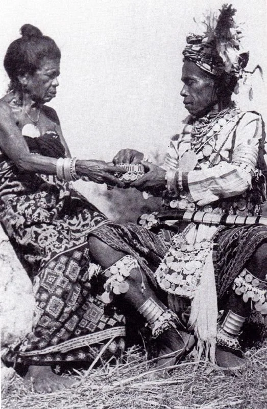 Deux personnes en tenue traditionnelle africaine échangeant un objet lors d'une cérémonie.