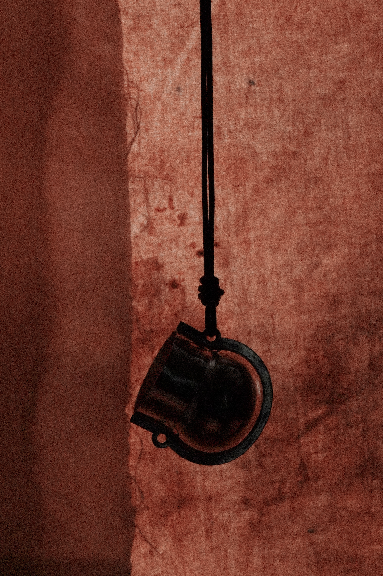 Une lampe suspendue en noir contre un mur rouge délavé.