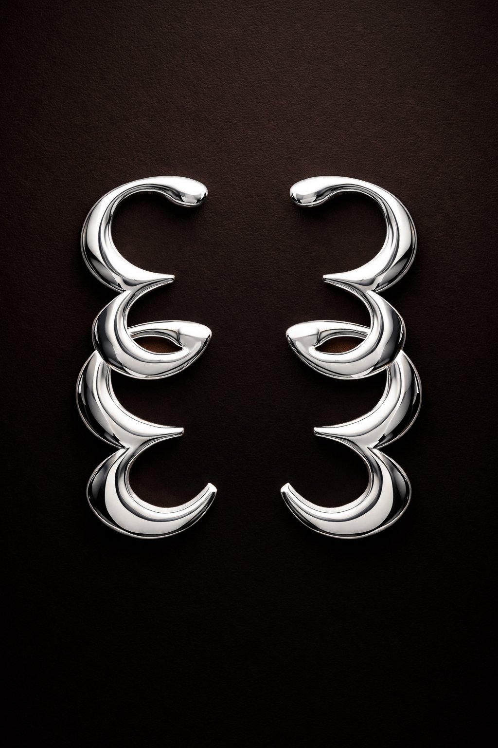 Boucles d'oreilles en forme de C en métal argenté, disposées symétriquement sur un fond noir.
