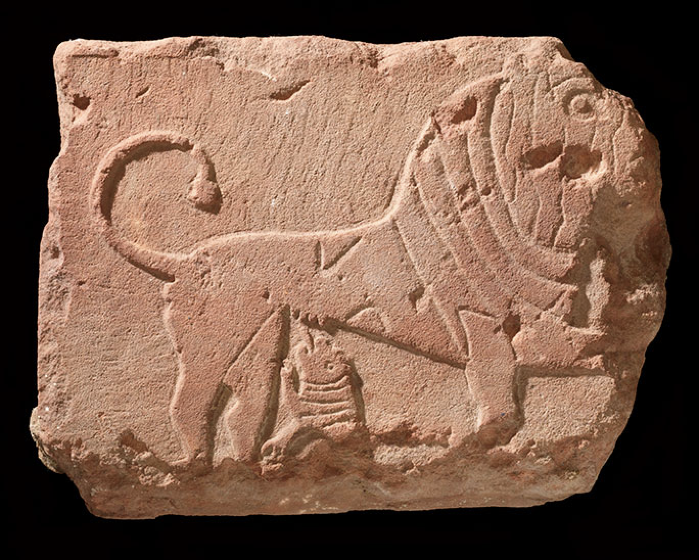 Une sculpture en pierre ancienne représentant un lion stylisé avec une tête détaillée et une queue courbée.