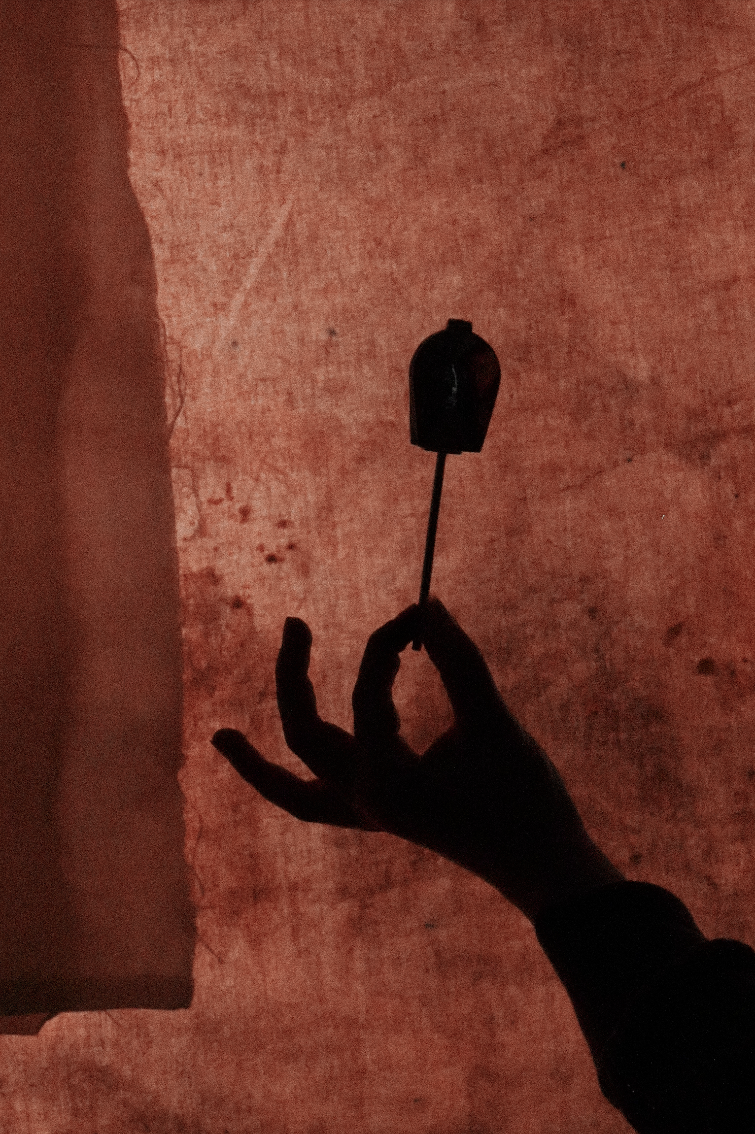 Silhouette d'une main tenant une souris d'ordinateur contre un mur rougeâtre.