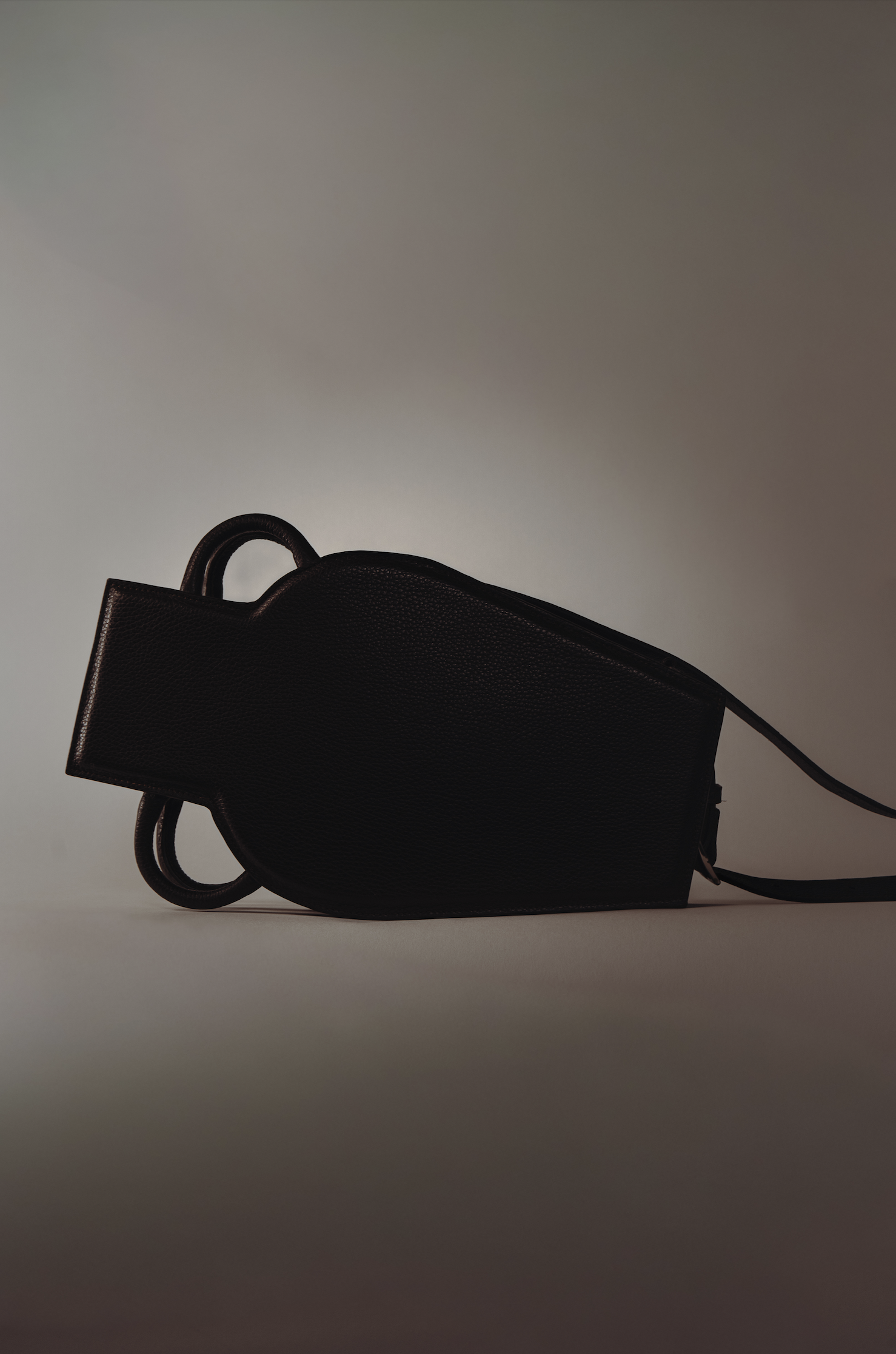 Une sac à main noir en cuir posé sur une surface claire contre un fond neutre.