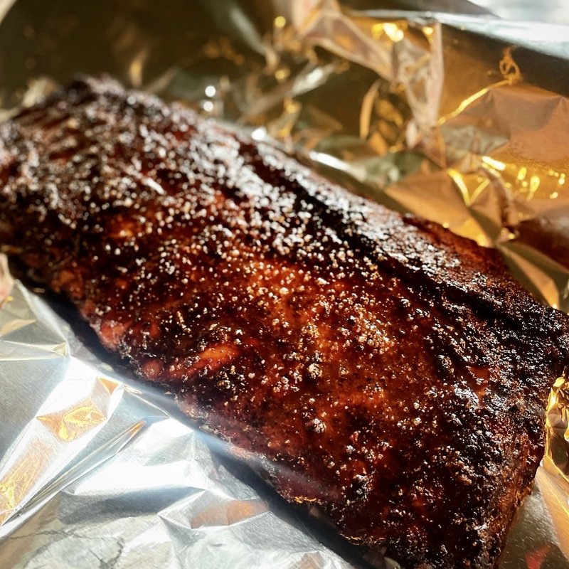 Barbecue ribs with a shiny glaze, sprinkled with some seasoning, resting on aluminum foil.