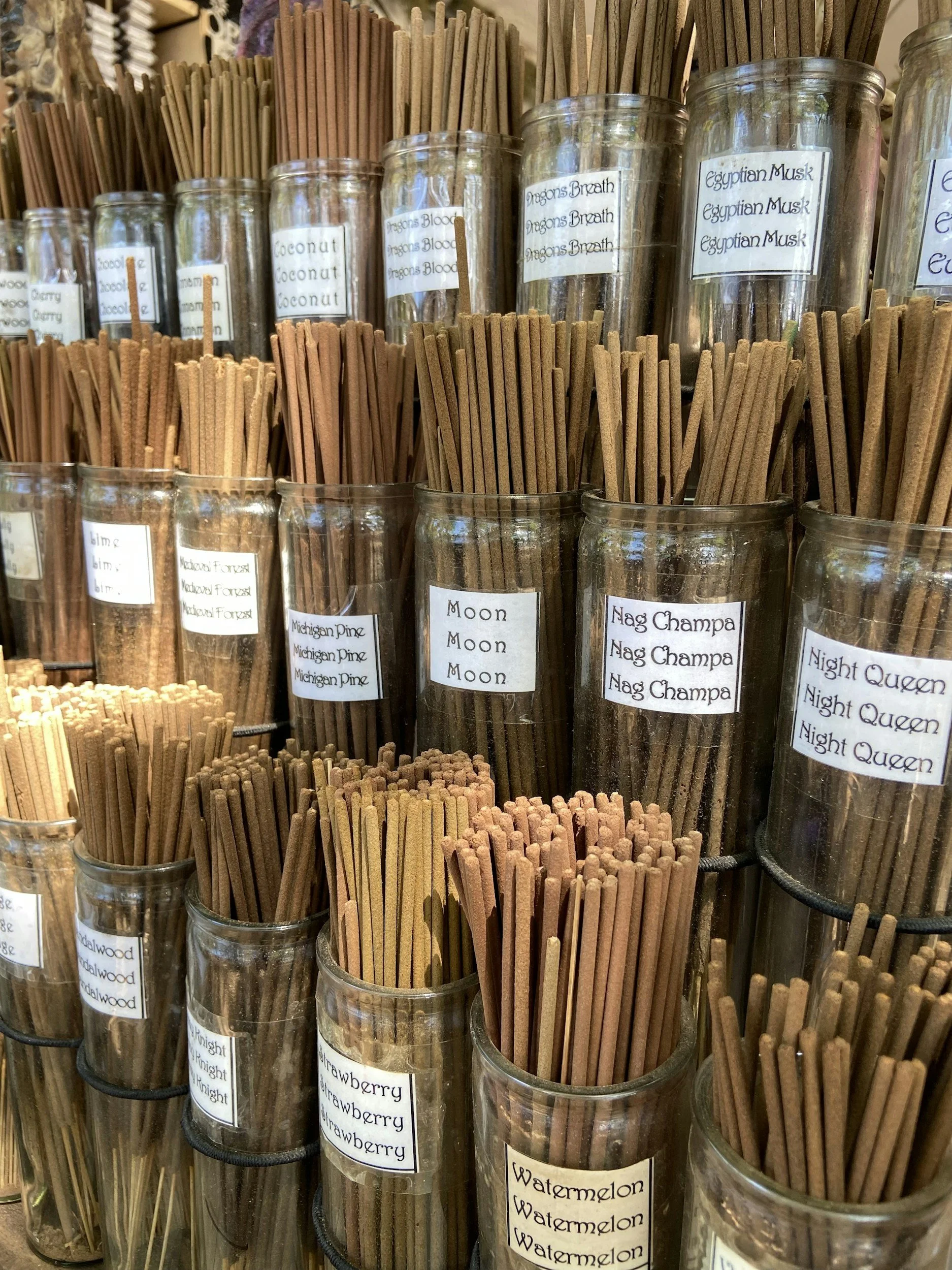 Multiple glass jars filled with various types of incense sticks labeled with different scents such as 'Dragon's Breath', 'Egyptian Musk', 'Moon', 'Nag Champa', and 'Watermelon'.