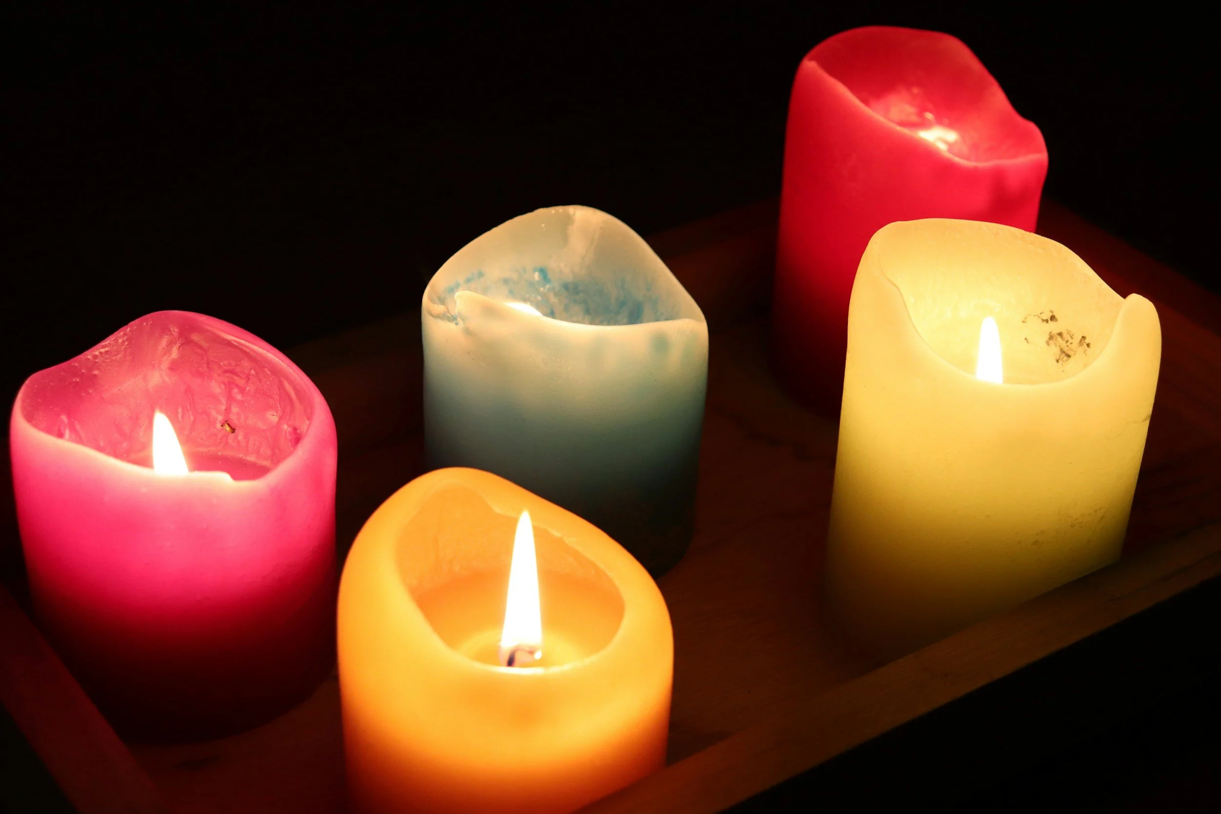 Colorful flameless candles in pink, blue, red, yellow, and orange are lit in a dark room, creating a cozy ambiance.