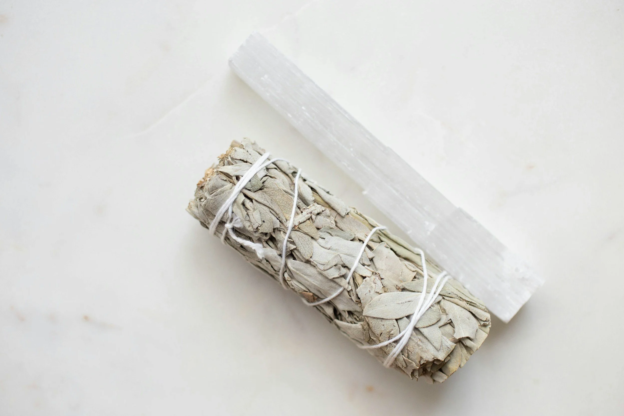 A bundle of sage smudge sticks tied with white string resting on a white surface.