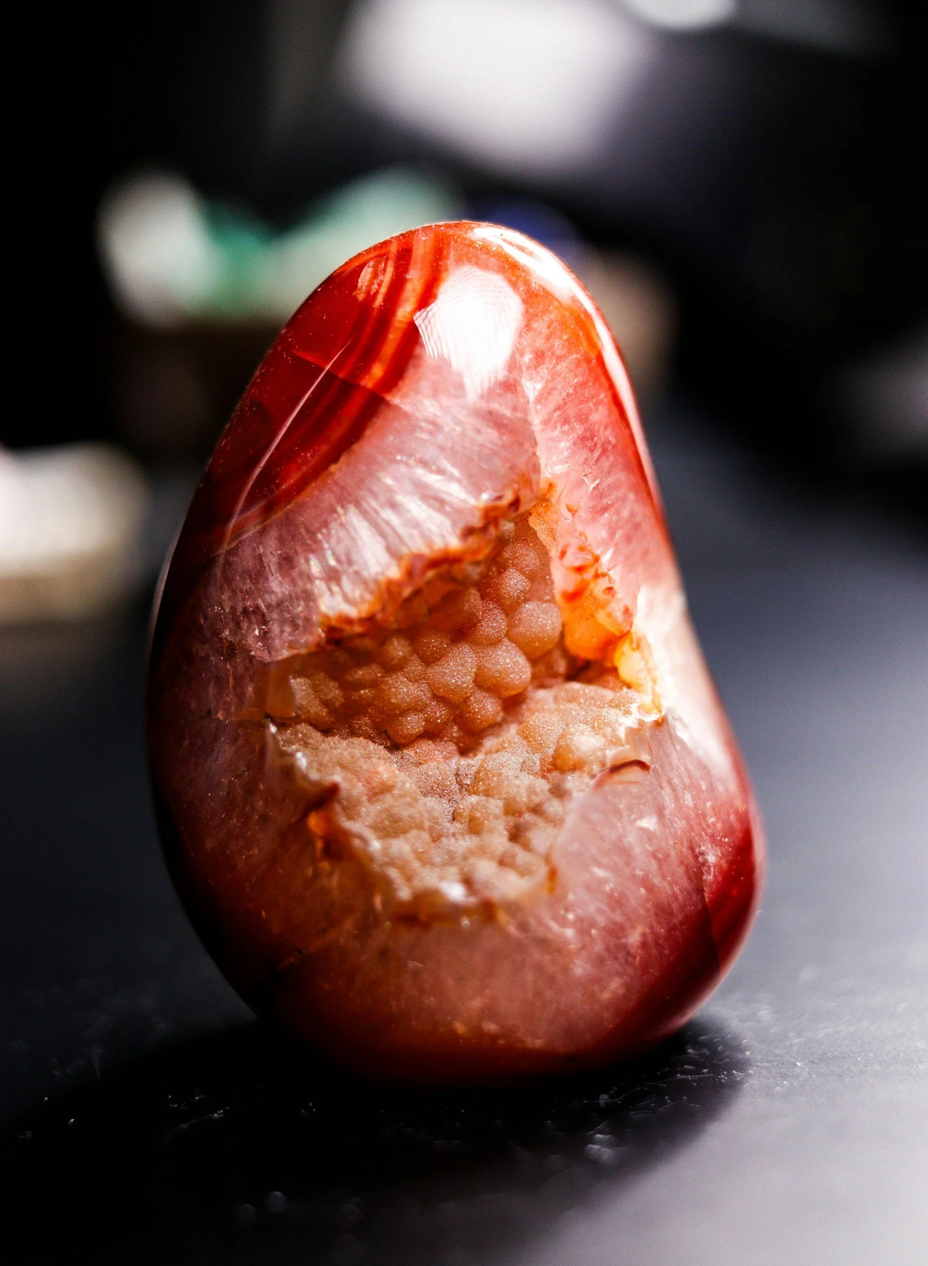 Close-up of a red date palm fruit with a shiny surface, showing its interior with small seeds, placed on a dark surface with a blurred background.