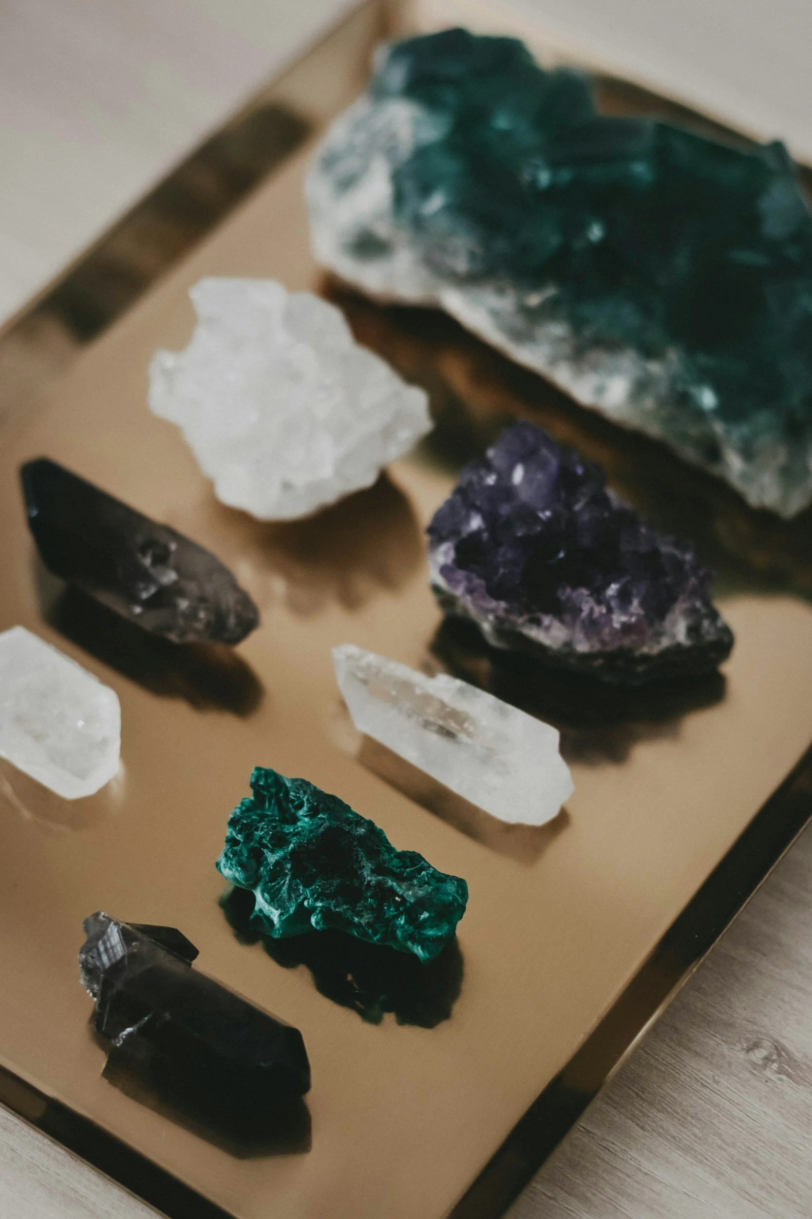 A display of various mineral and crystal specimens on a beige table, including a large dark green mineral, a white mineral, and smaller purple, black, and green minerals.